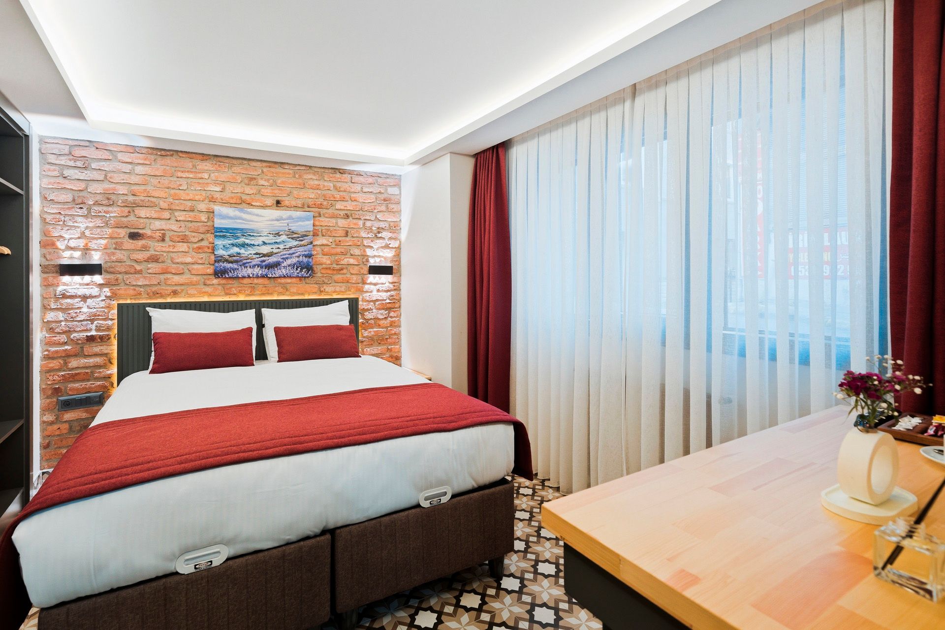 ARTELIST HOTEL | Modern bedroom with red accents, brick wall, bed, desk, and large window curtains
