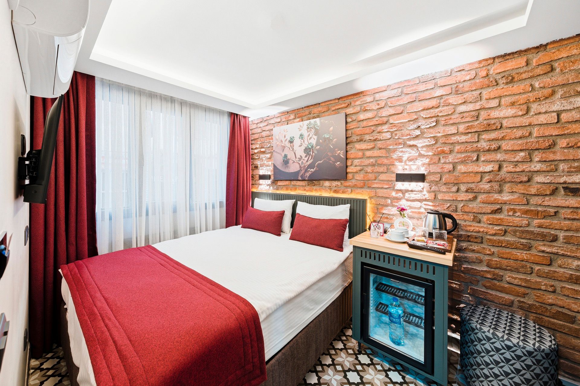 ARTELIST HOTEL | Modern bedroom with red accents, exposed brick wall, white bed, and small blue cabinet