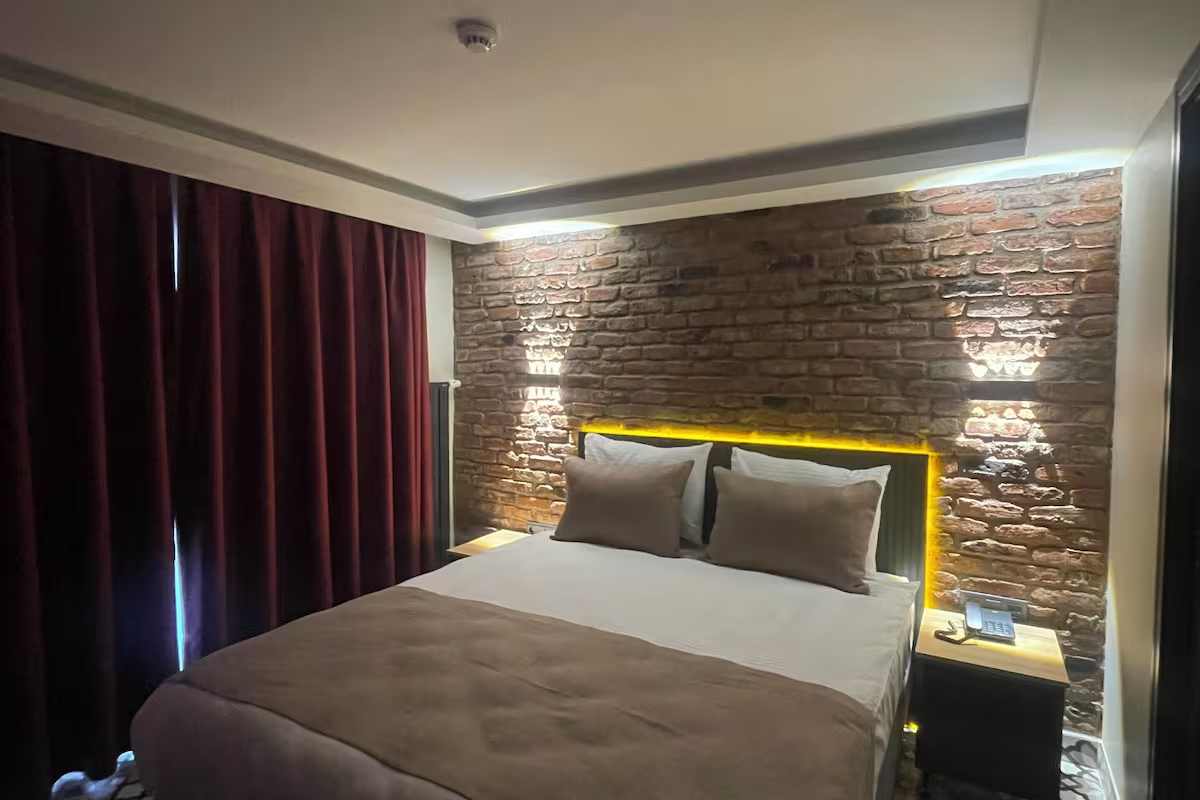ARTELIST HOTEL | Modern hotel room with a bed, stone accent wall, warm lighting, and dark curtains