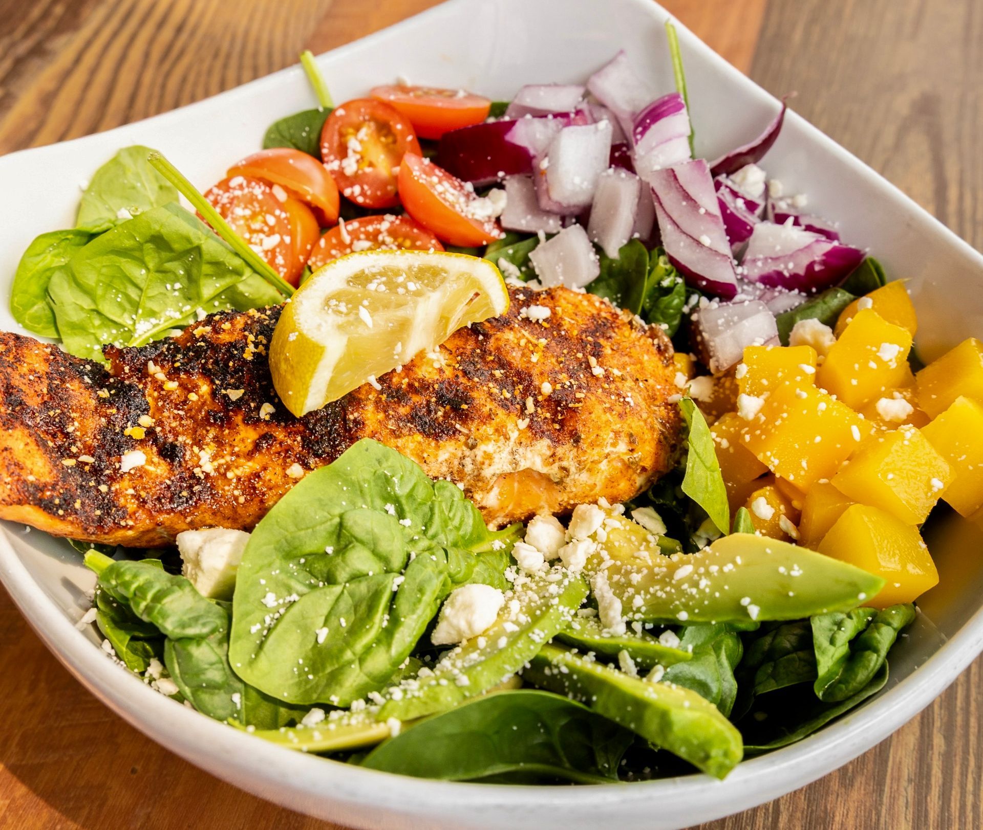 Grilled chicken salad with lettuce, cucumber, mango, onion, and lemon wedge in a white bowl