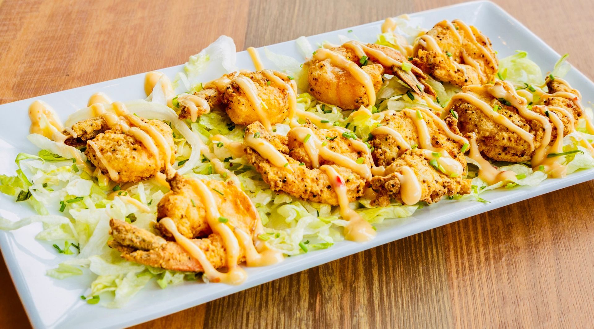 Plated salad topped with grilled shrimp and orange dressing on a white rectangular dish