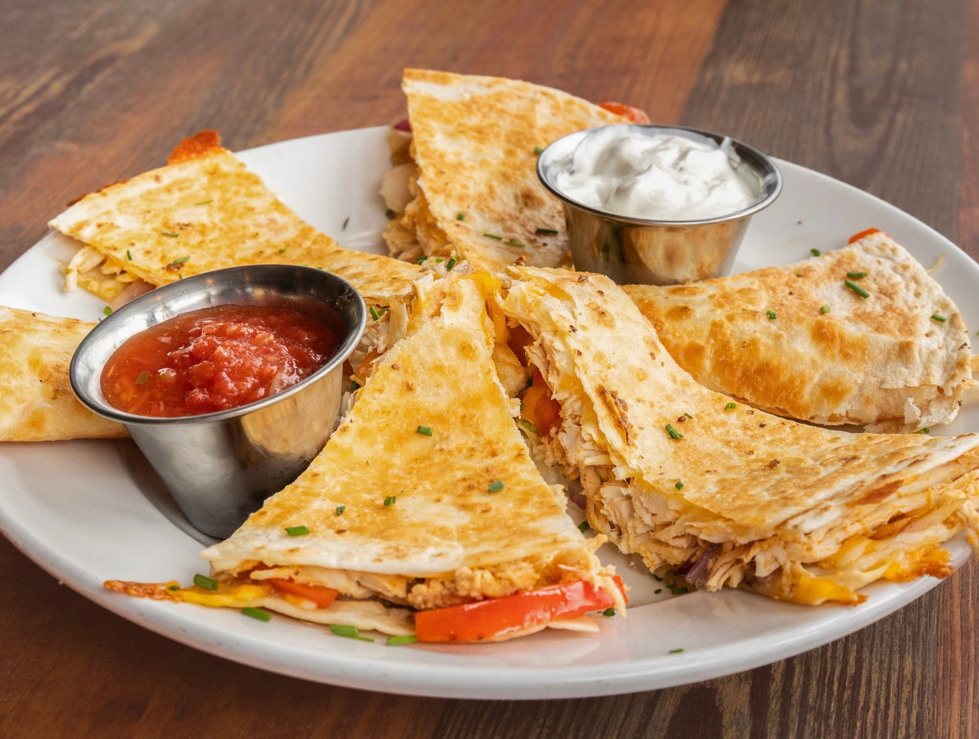 Plate of triangular quesadillas with salsa and sour cream on a wooden table