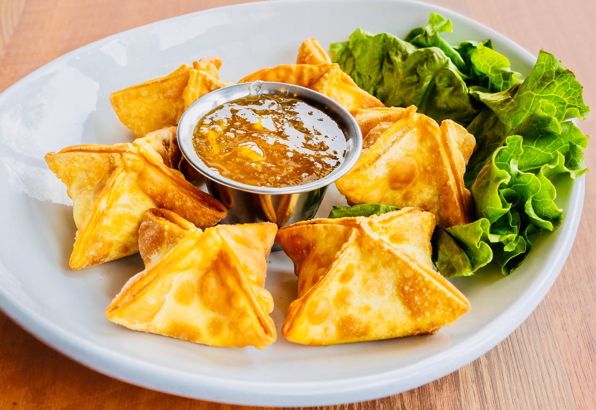 Plate of golden fried dumplings with dipping sauce and lettuce garnish