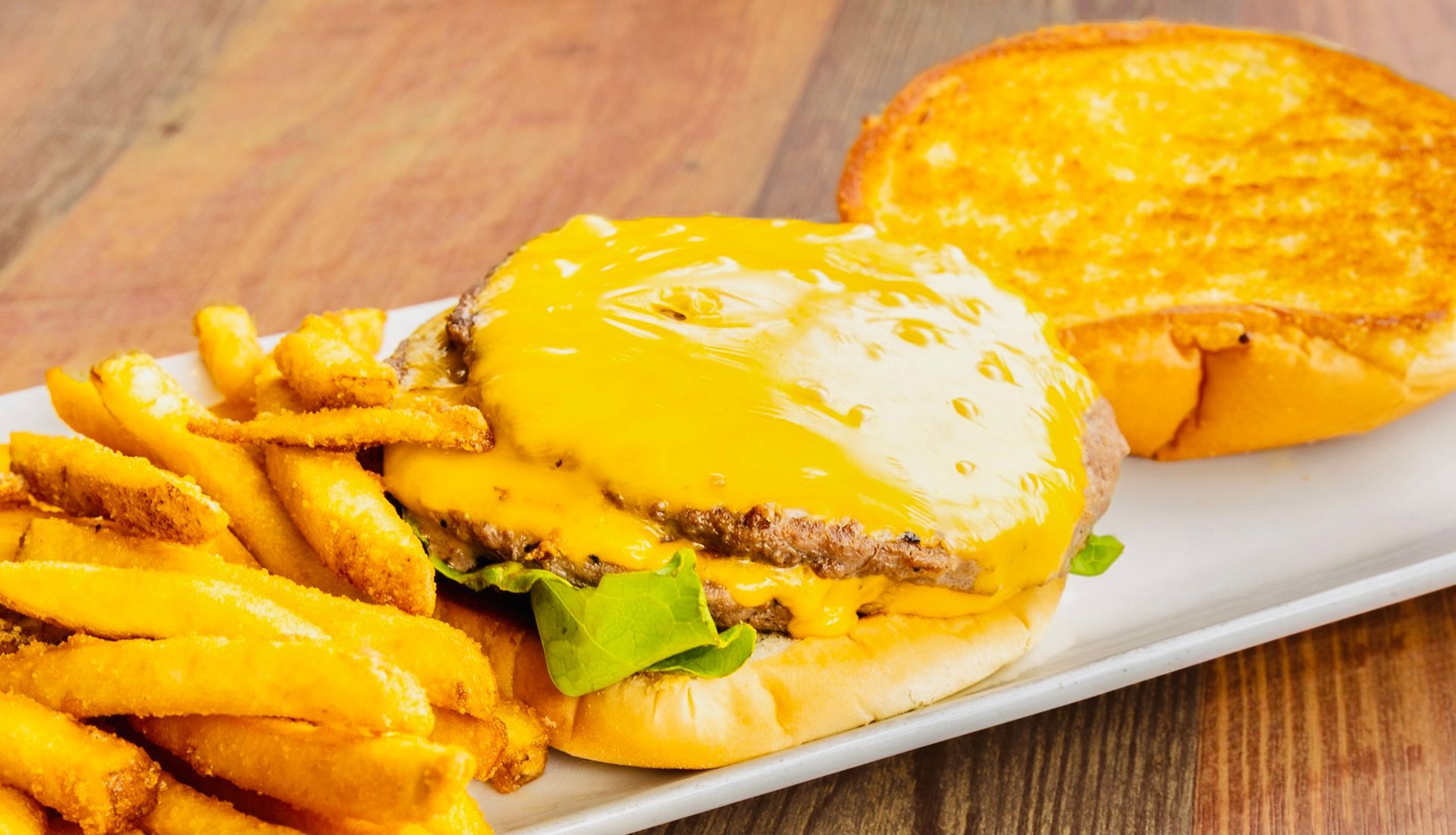 Cheeseburger with melted cheese and fries on a white plate on a wooden table