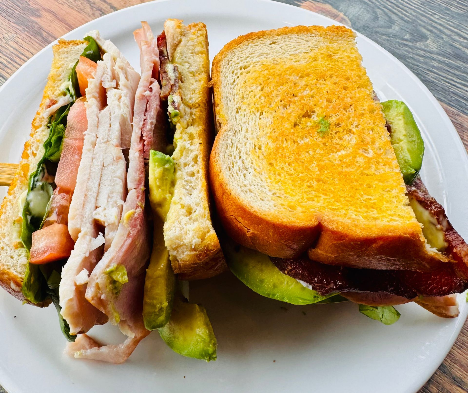 Club sandwich with toasted bread, bacon, lettuce, and avocado on a white plate