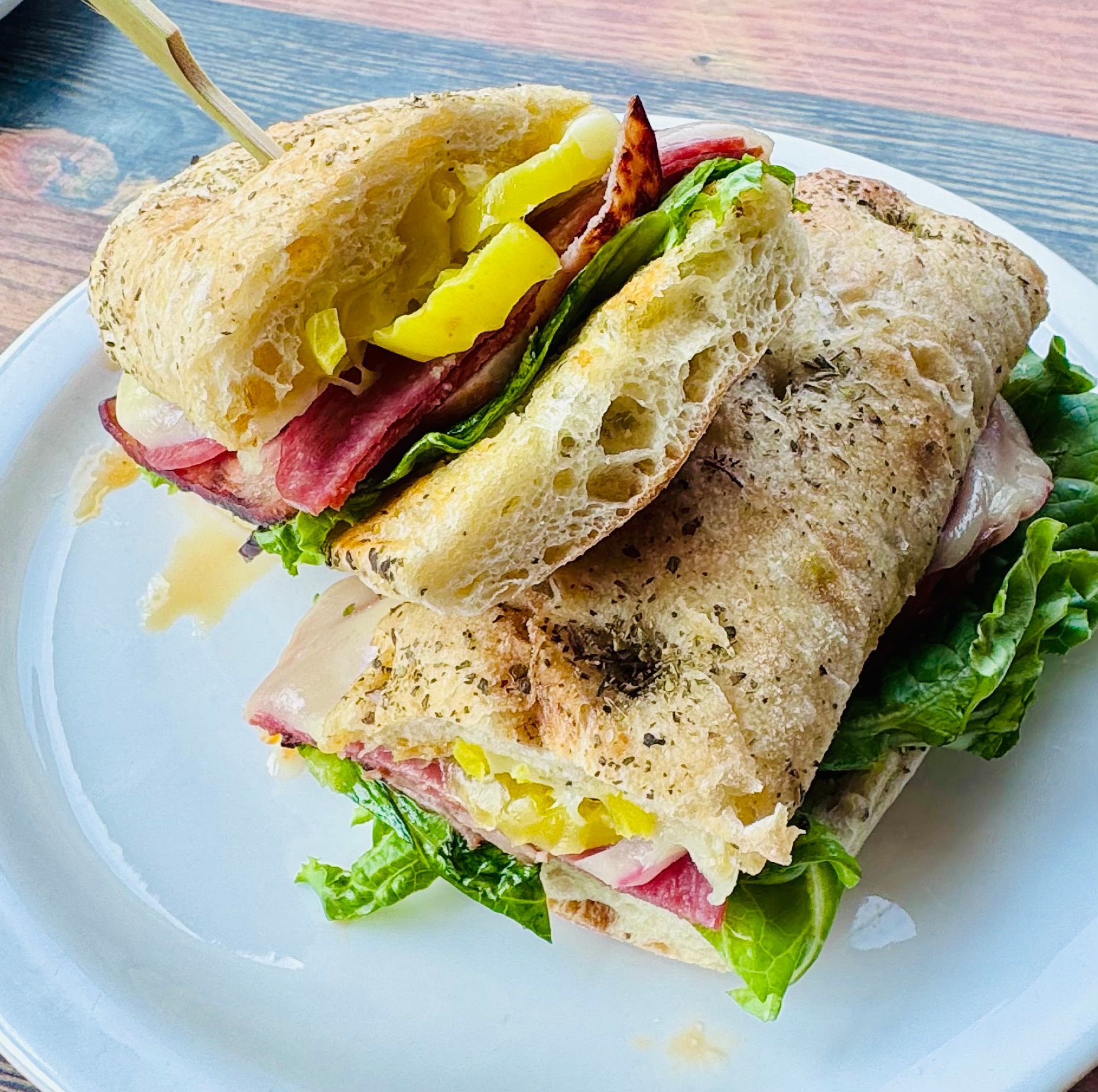 Two stacked sandwich halves with lettuce, meat, yellow peppers, and toasted bread on a blue table