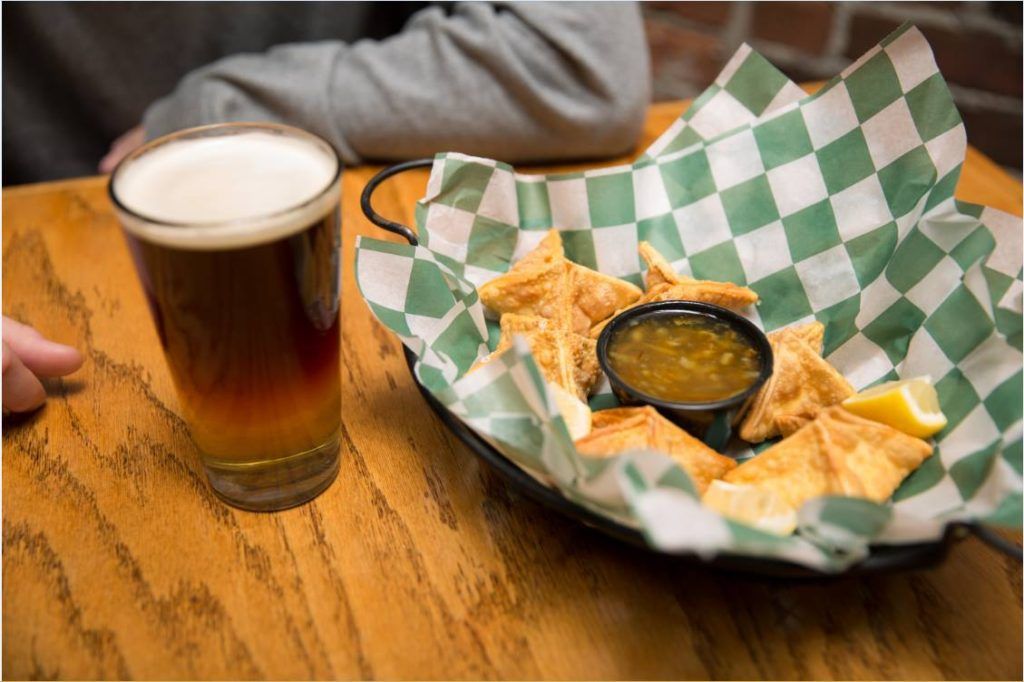 A person is sitting at a table with a bowl of chips and a glass of beer.