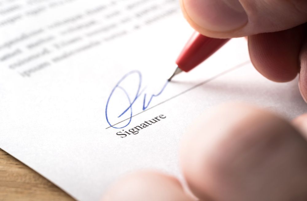 A Person is Signing a Document With a Red Pen — Clarence Property Consultants In South Grafton, NSW
