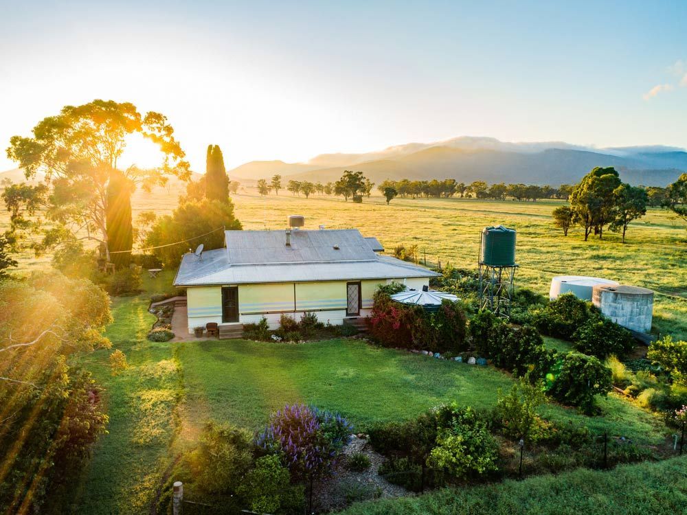 An Aerial View of a House in the Middle of a Grassy Field at Sunset — Clarence Property Consultants In Maclean, NSW