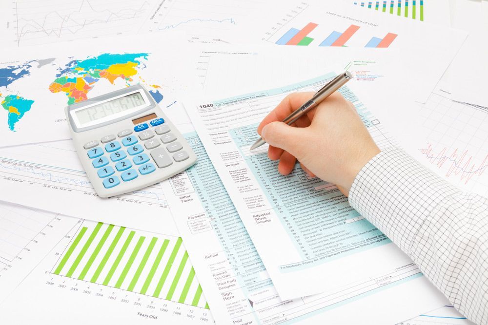 A Calculator and a Hand Holding a Pen Completing a Tax Form — Clarence Property Consultants In Grafton, NSW
