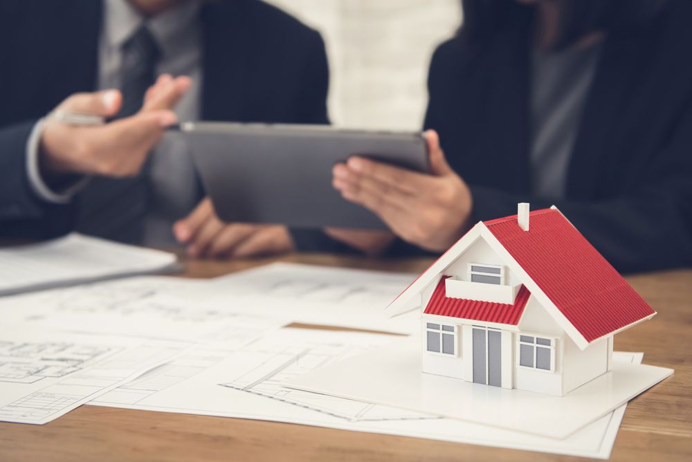 A Couple of People Are Sitting at a Table With a Model House and a Tablet — Clarence Property Consultants In Yamba, NSW