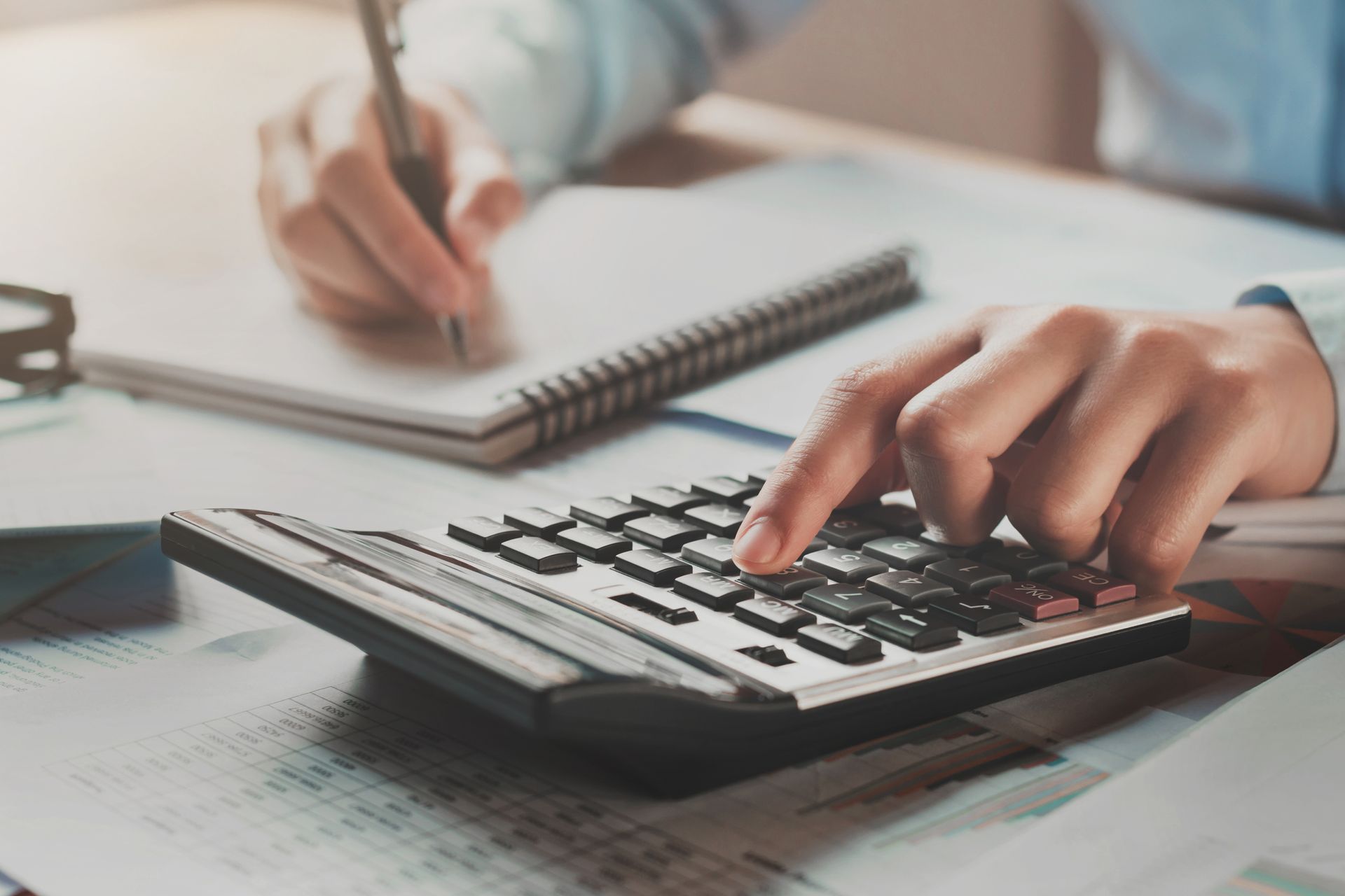 Una persona está escribiendo en un cuaderno mientras usa una calculadora .