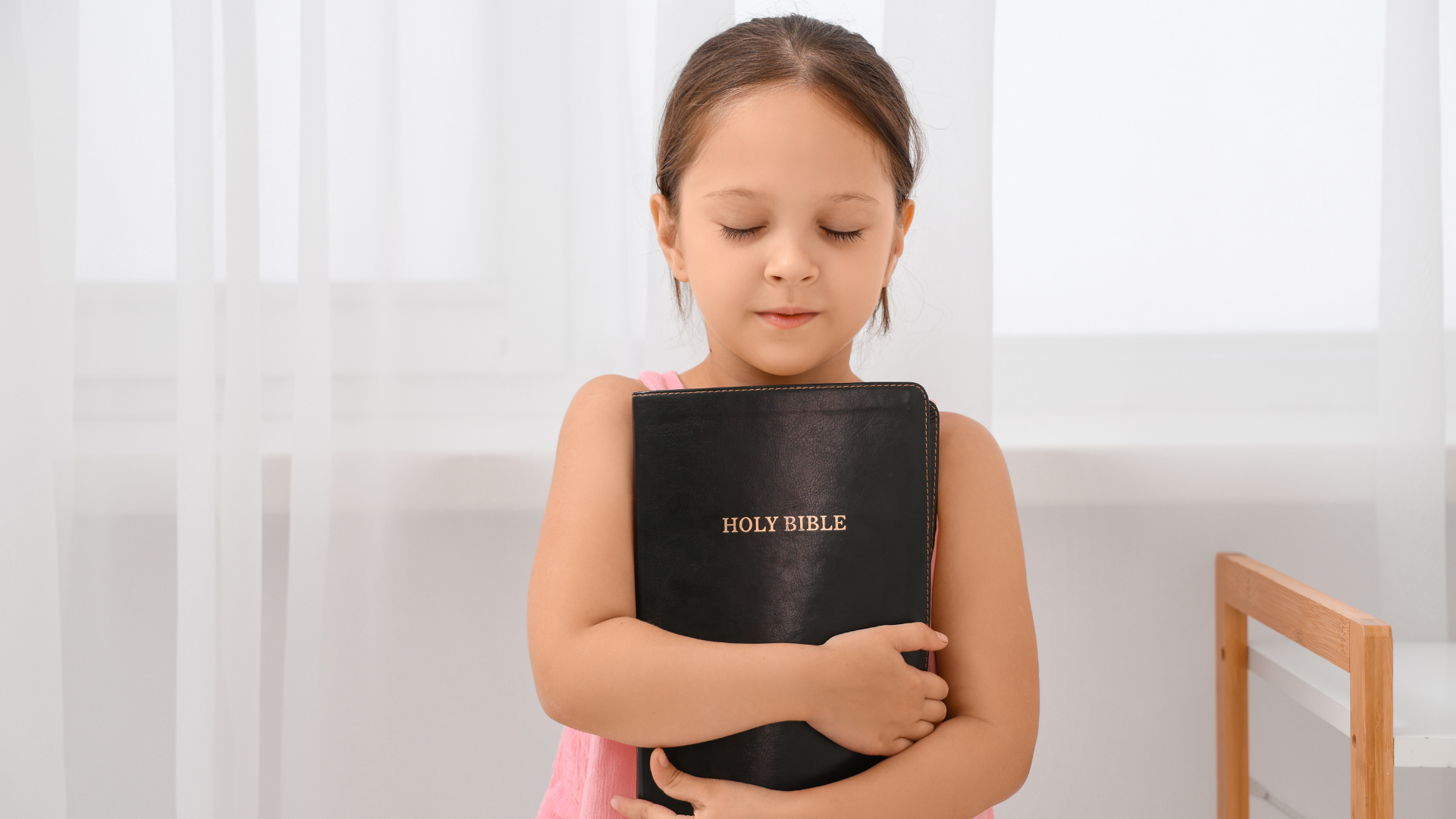 Girl holding a black notebook while standing by a window in a bright room