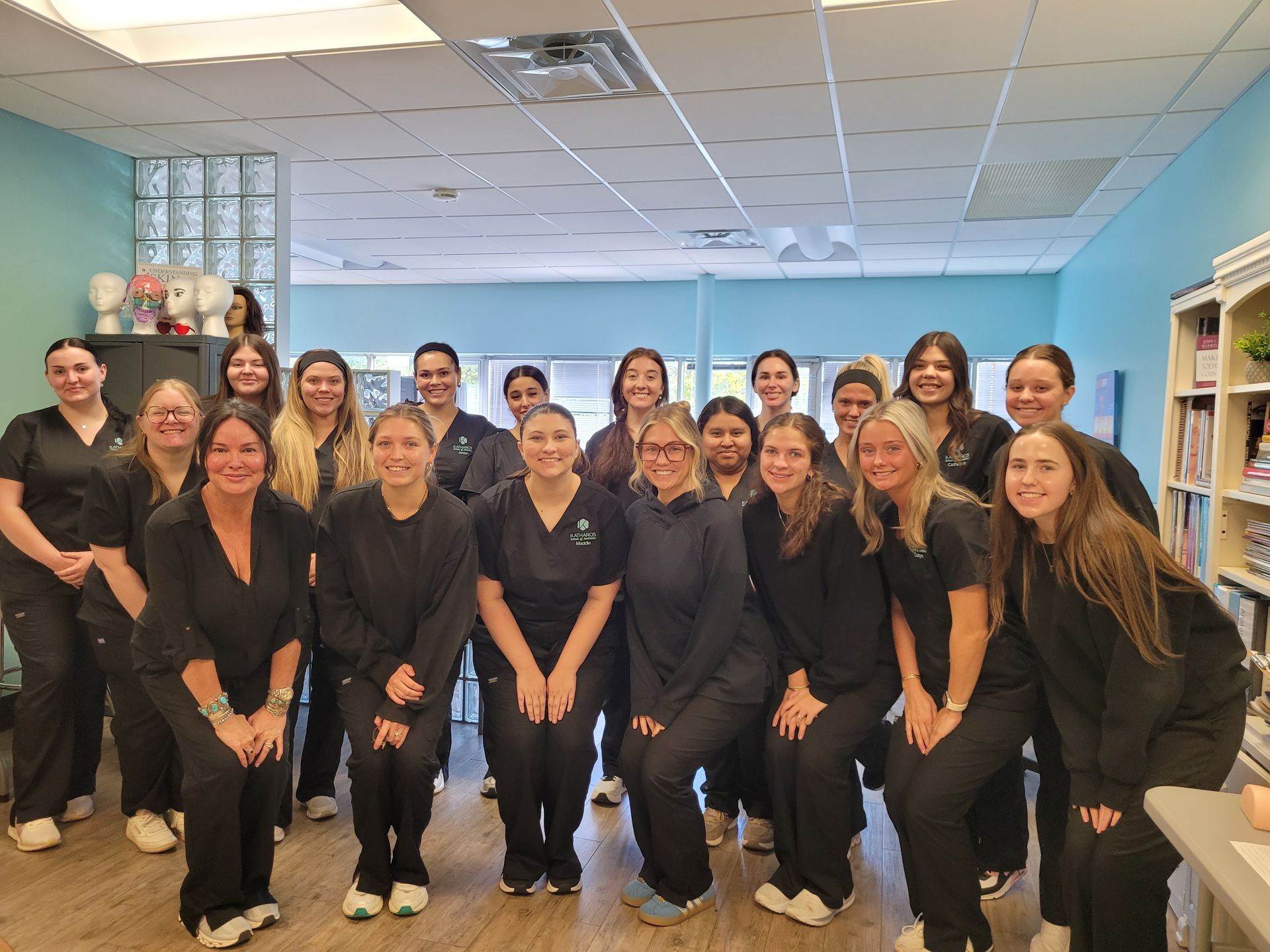 Group of healthcare staff in black scrubs posing in a clinic room with blue walls and white ceiling lights