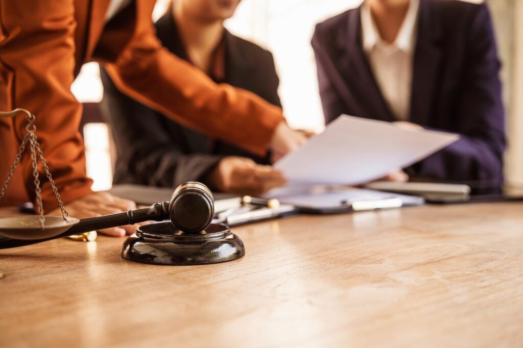 Gavel on Wooden Table With Law Team Reviewing Documents; Scales of Justice — Bradley Solicitors in Larrakeyah, NT