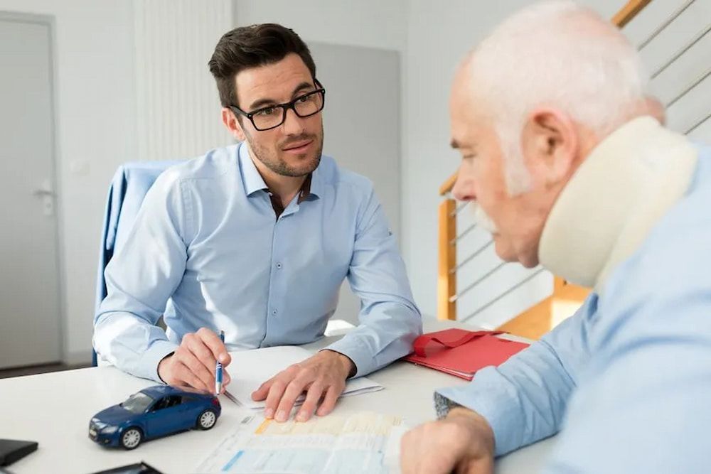 Man in Glasses Reviews Documents With a Man Wearing a Neck Brace, a Toy Car — Bradley Solicitors in Larrakeyah, NT