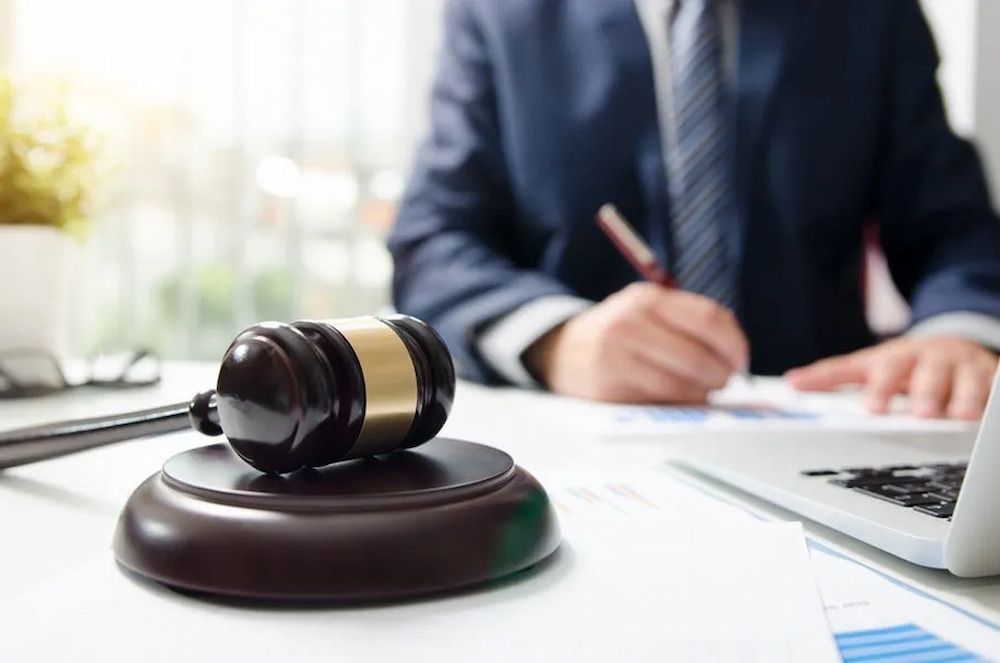 Gavel on Desk in Front of a Person in a Suit, Writing on Documents Near a Laptop — Bradley Solicitors in Larrakeyah, NT
