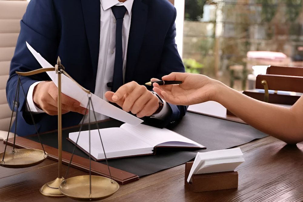 Lawyer in Suit Handing Paperwork to Person Holding Pen; Scales of Justice on Desk — Bradley Solicitors in Larrakeyah, NT