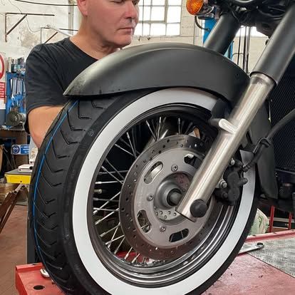 Ruota anteriore di motocicletta con parafango nero, forcella argentata e un meccanico sullo sfondo.