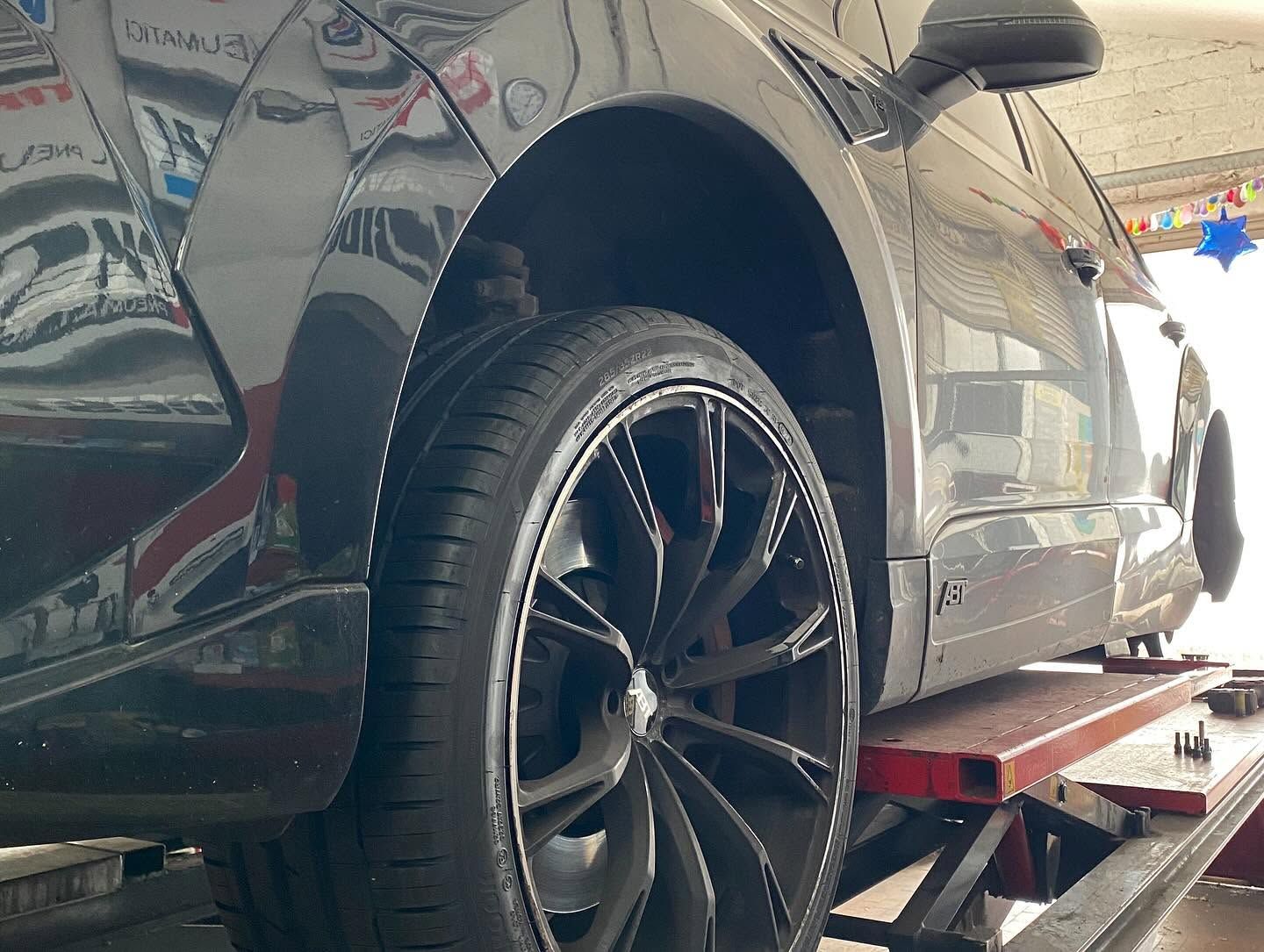 Primo piano della ruota posteriore di un'auto nera su un ponte sollevatore in un garage, con una piattaforma rossa sottostante.