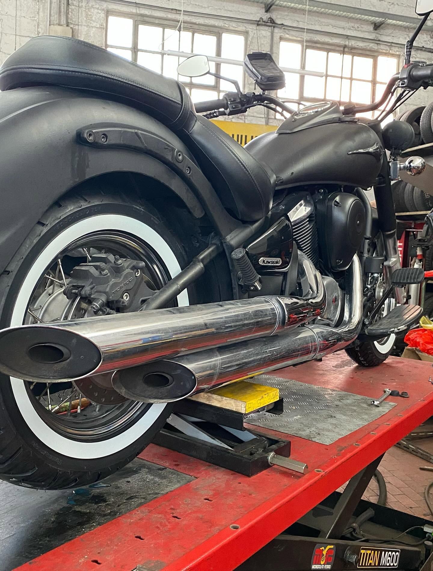 Una motocicletta nera su un ponte sollevatore rosso in un'officina, che mostra i tubi di scarico cromati e gli pneumatici con fascia bianca.