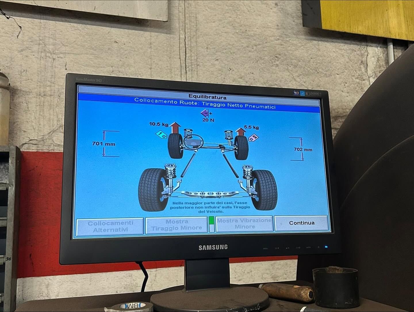 Monitor che mostra uno schema di allineamento di un veicolo con quattro ruote su schermo blu in un'officina.