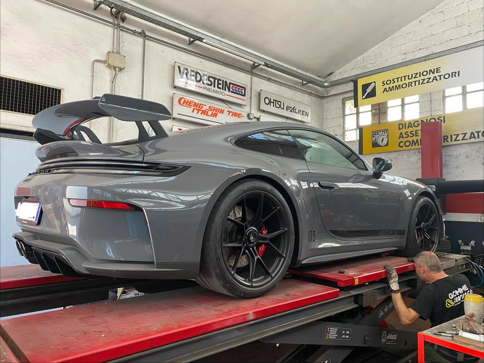 In un'officina, un'auto sportiva grigia si trova su un banco dinamometrico, con un tecnico al lavoro vicino alla ruota posteriore.