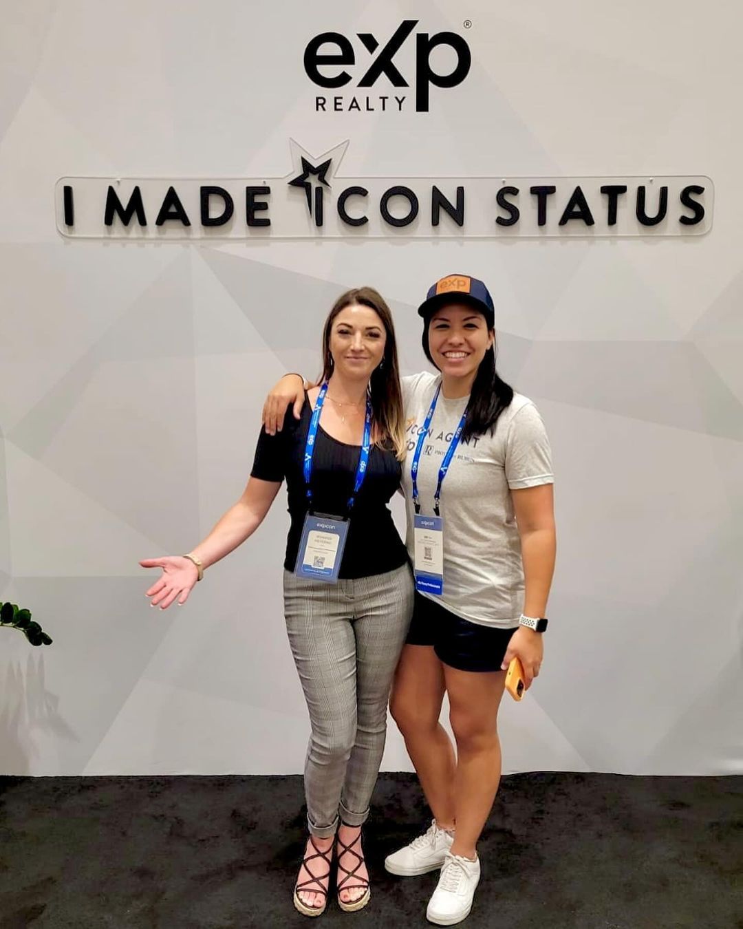 Two women posing in front of an eXp Realty sign that reads “I MADE ICON STATUS.”