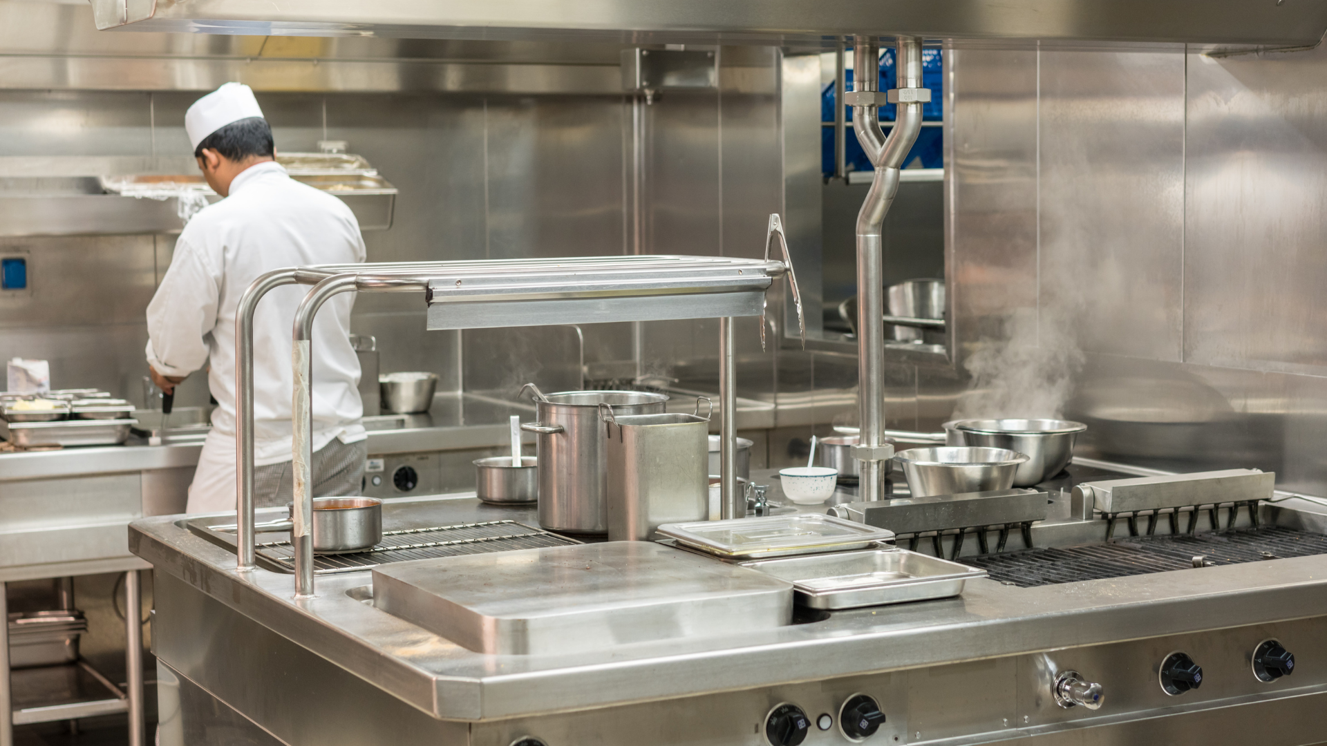 Chef working in a stainless steel commercial kitchen beside industrial cooking equipment