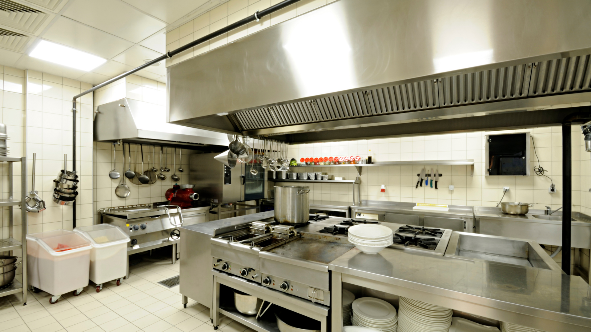 Commercial stainless-steel kitchen with stove, ovens, prep counters, and large exhaust hood