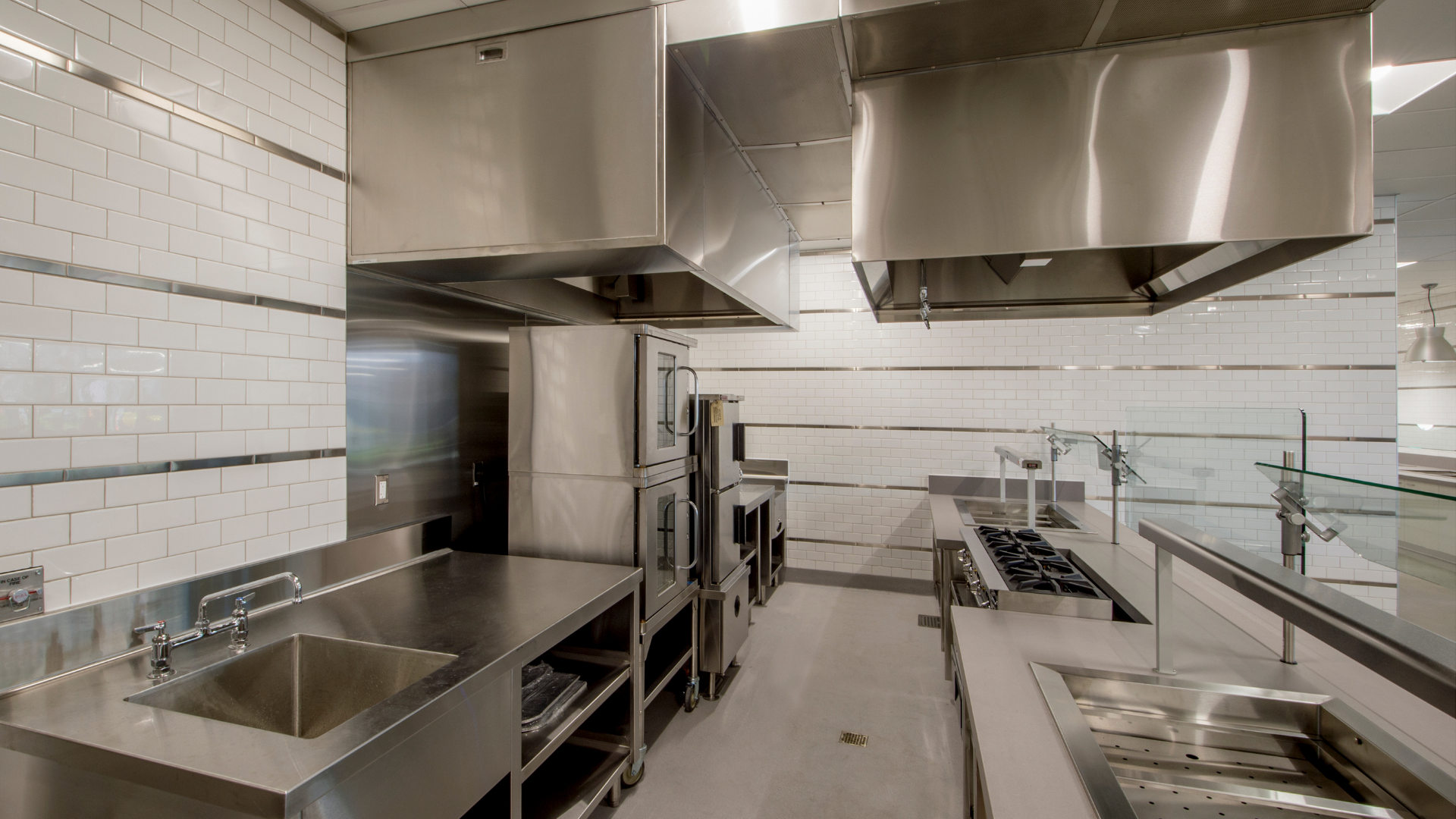 Modern commercial kitchen with stainless steel counters, ventilation hoods, and a wooden prep island with ingredients