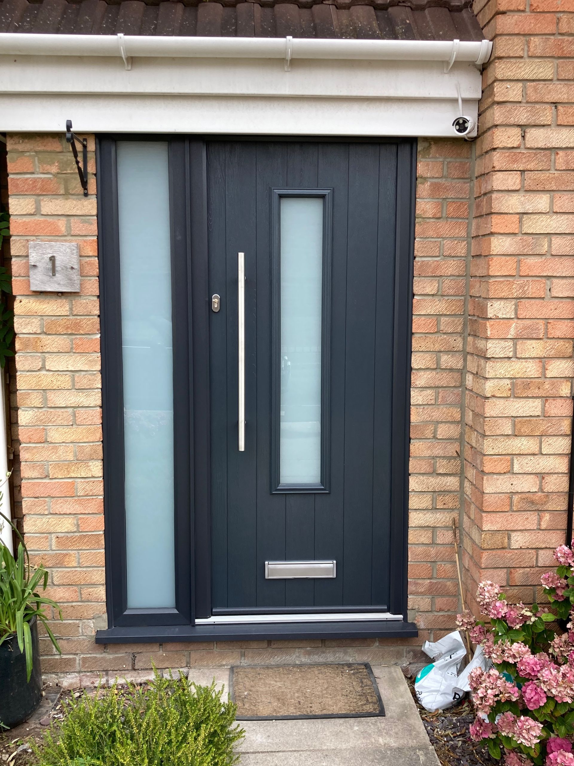 A black front door with a stainless steel handle is on a brick building.