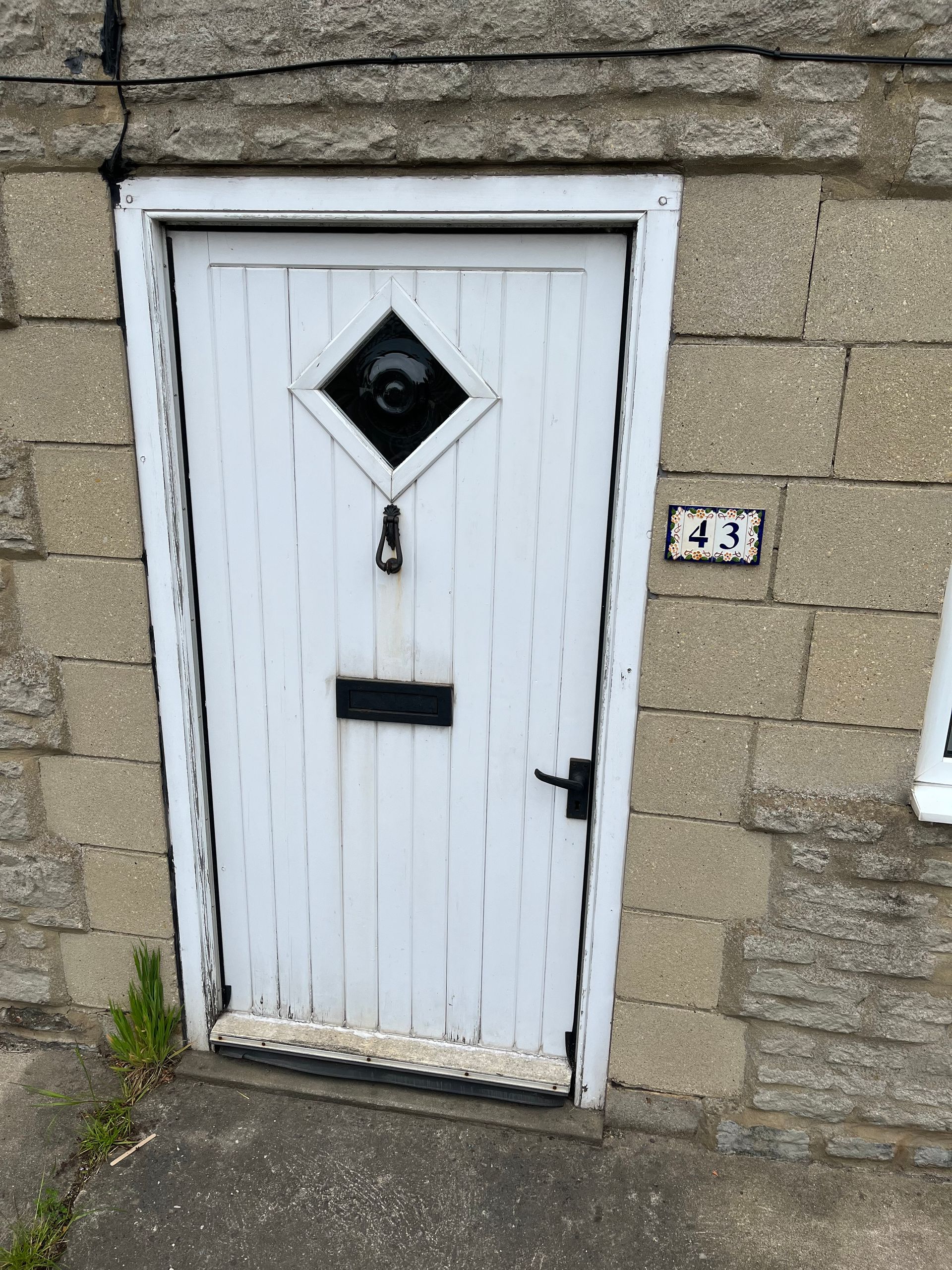 A white door with a diamond shaped window is on a brick wall.