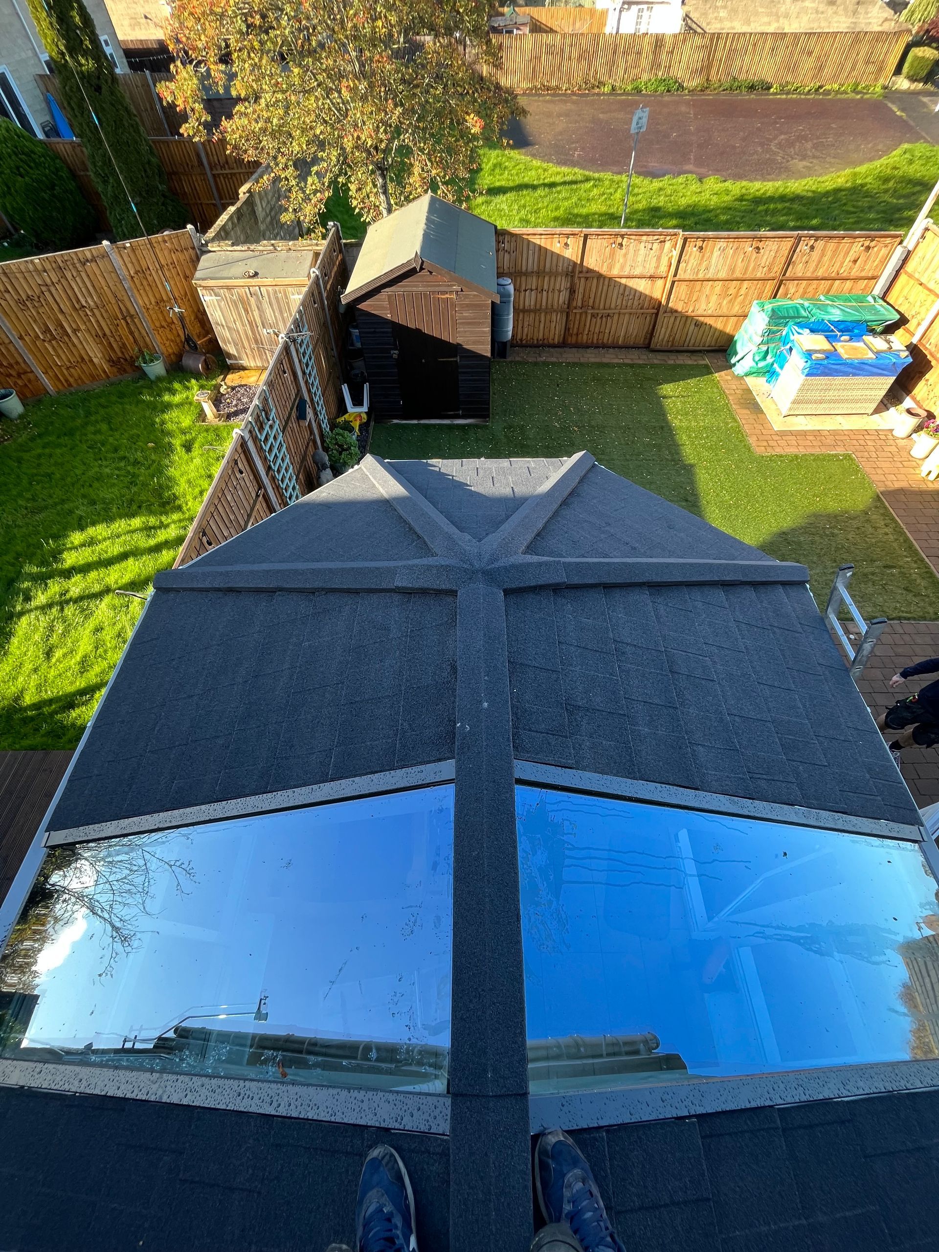 A person is standing on top of a roof looking down at a backyard.