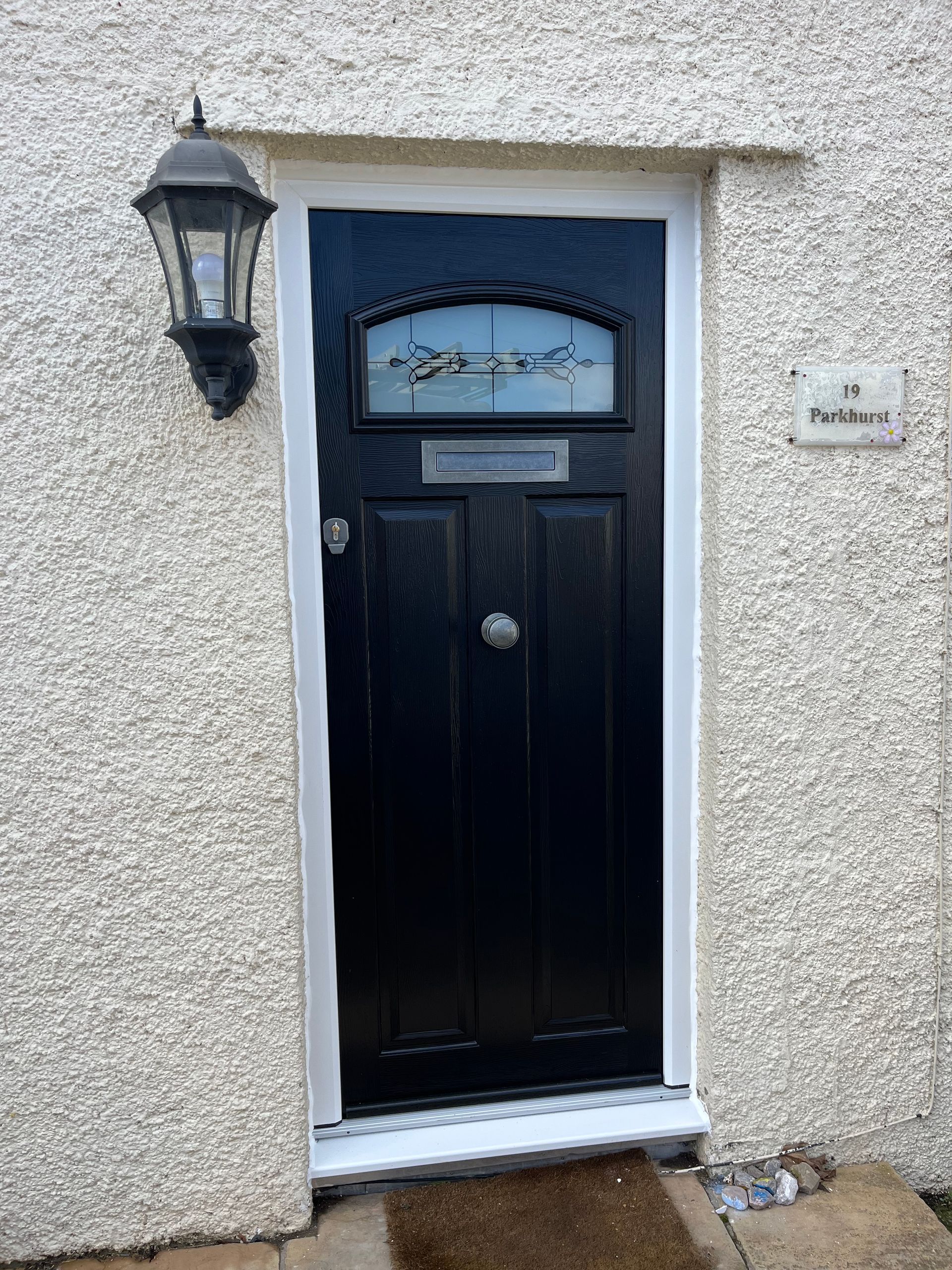 A black front door with a white trim and a lamp on the side of a house.