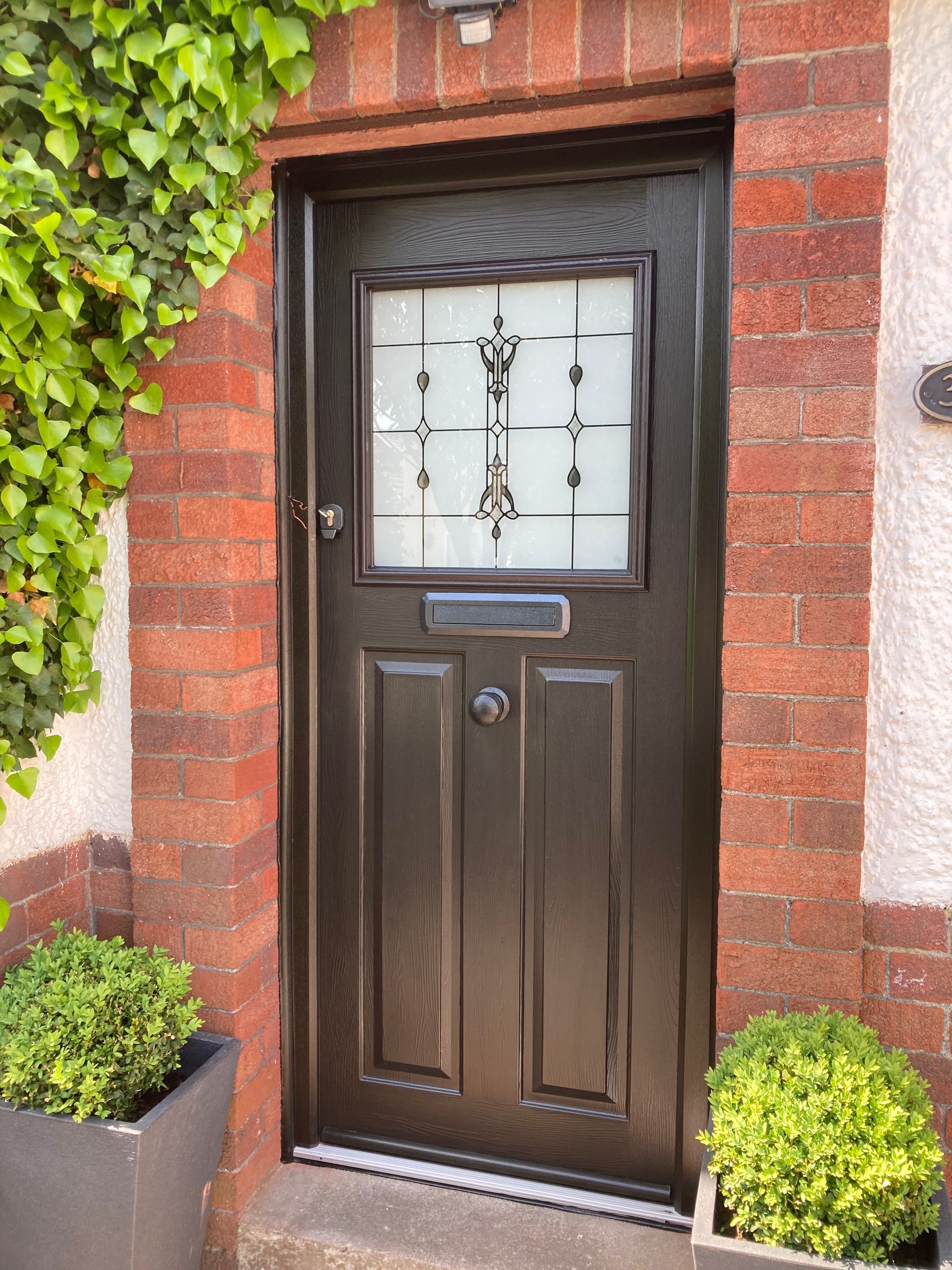 A black door is sitting on a brick wall next to a potted plant.