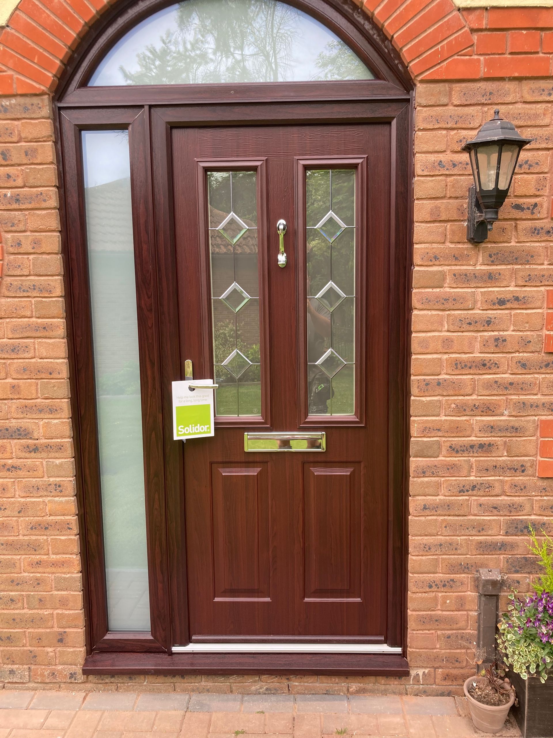 A brown front door with a brick wall and a lamp on the side of it.