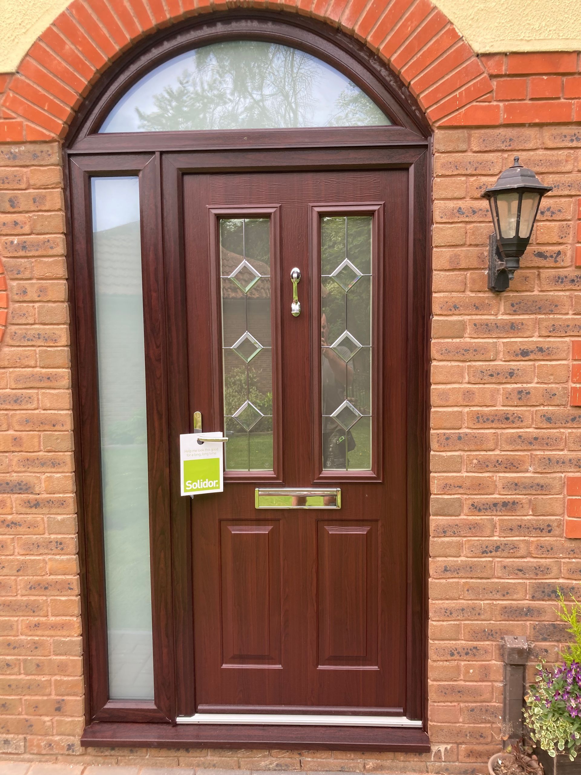 A brown door is on a brick wall with a lamp on the side.