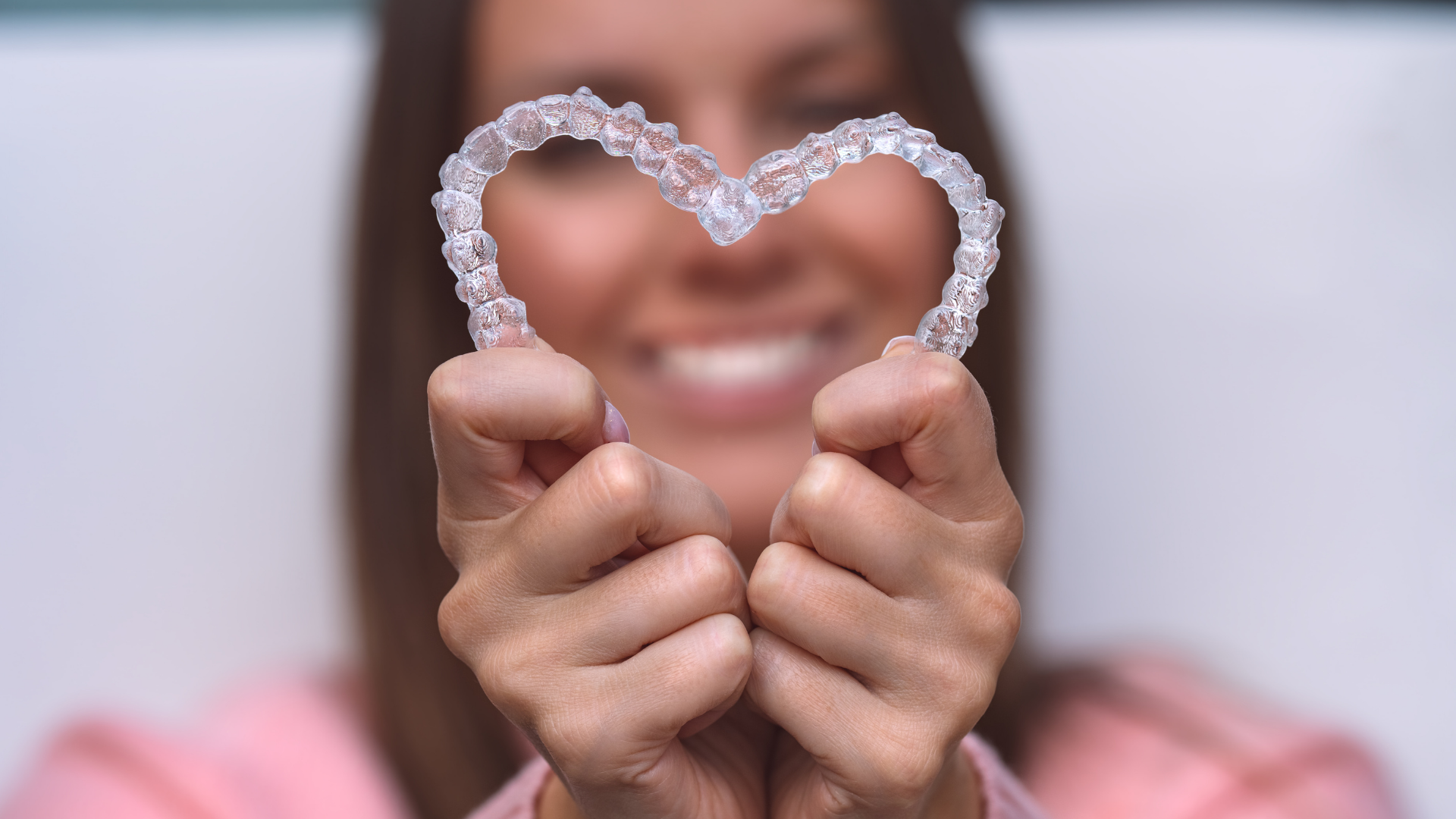 Woman holding clear teeth aligners in the shape of a heart, smiling.