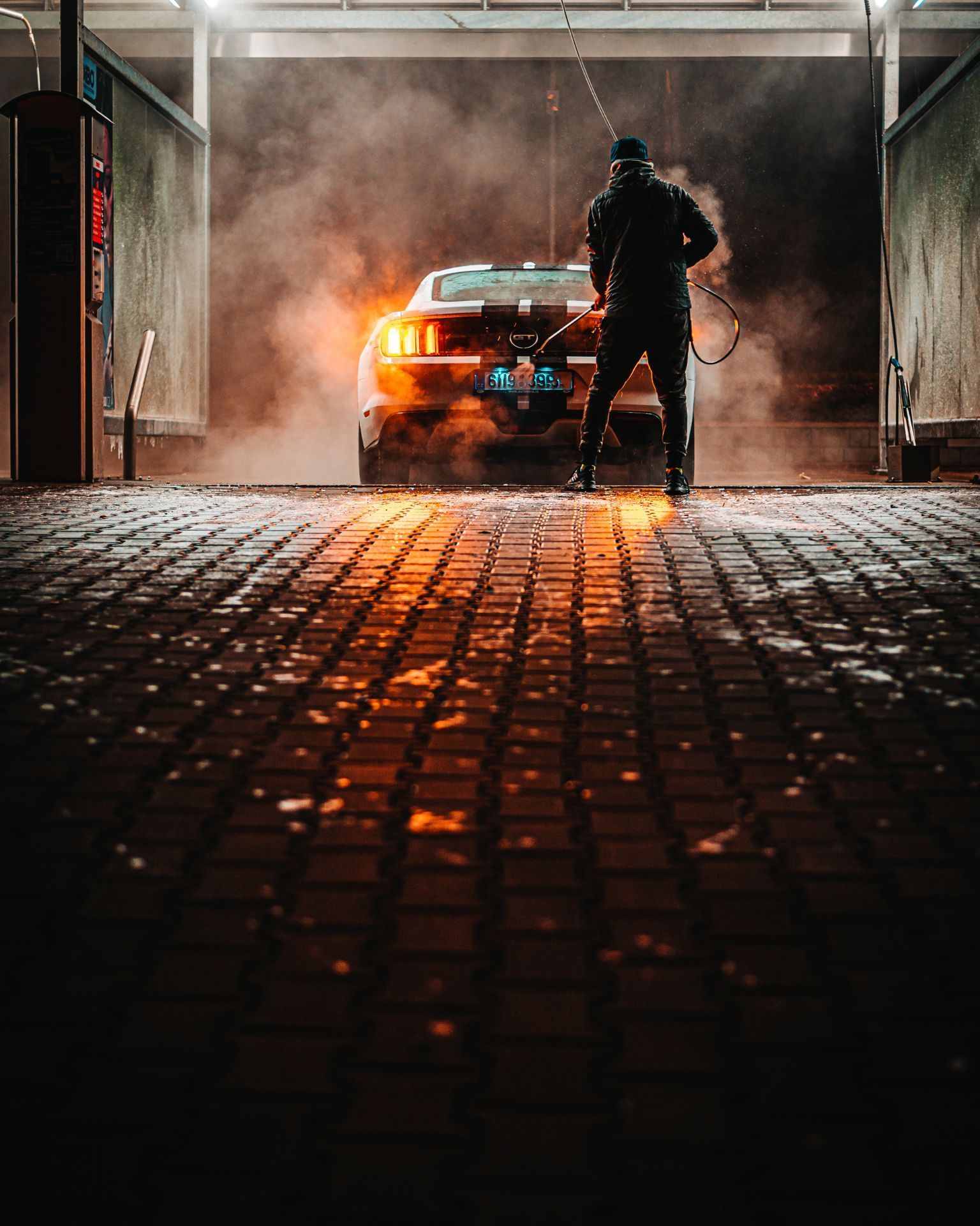 A man with tattoos is washing a car in a garage.