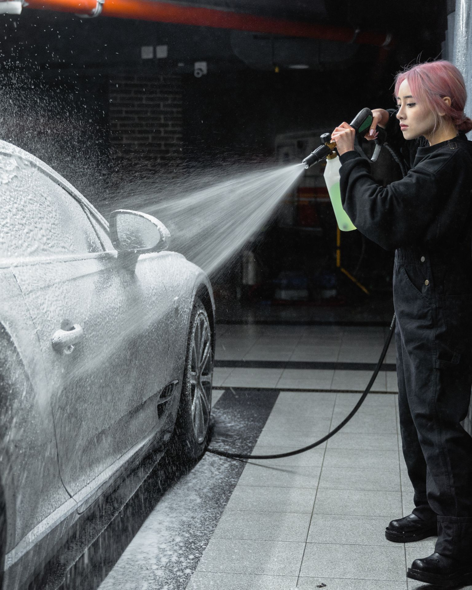 A man with tattoos is washing a car in a garage.
