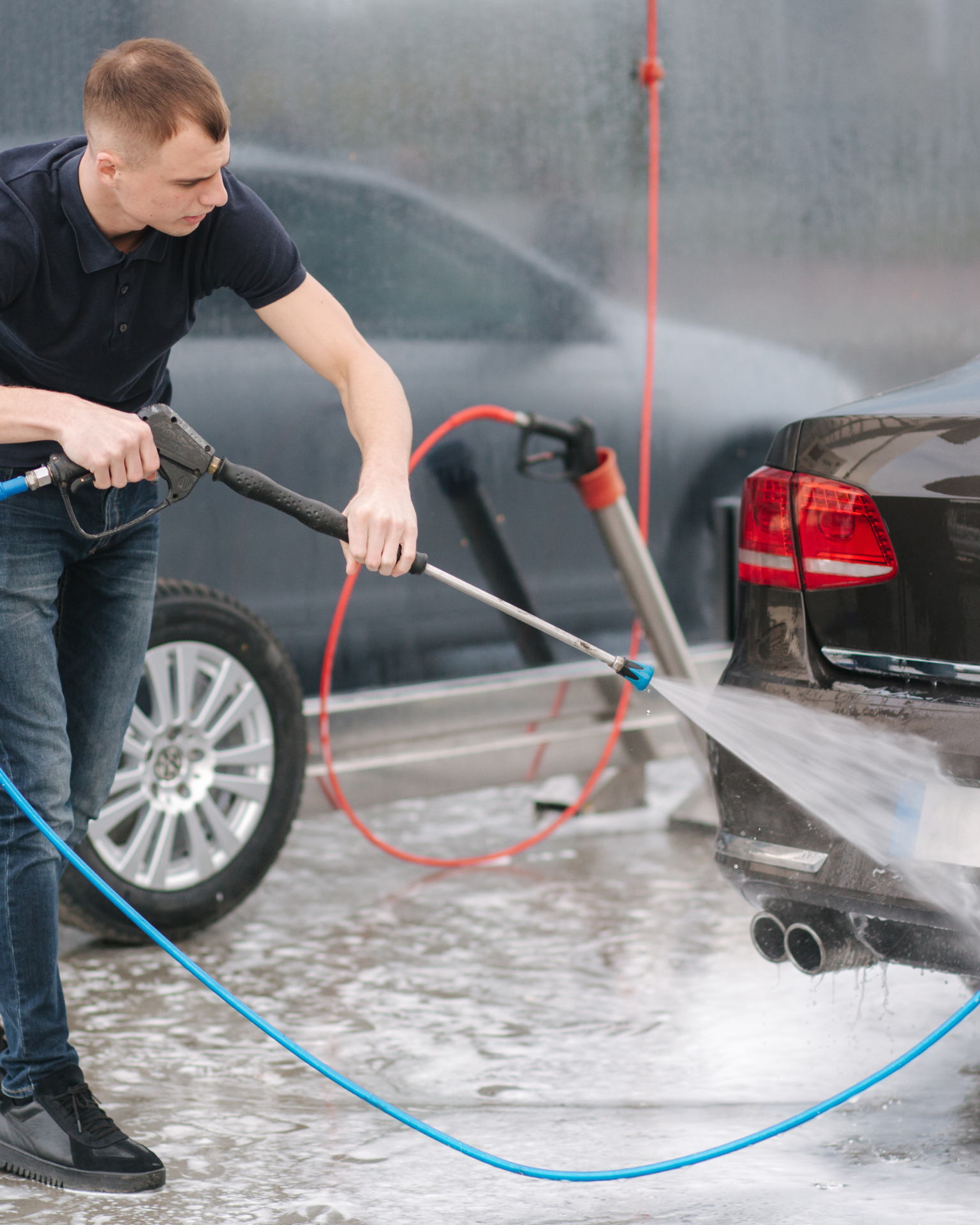 A man with tattoos is washing a car in a garage.