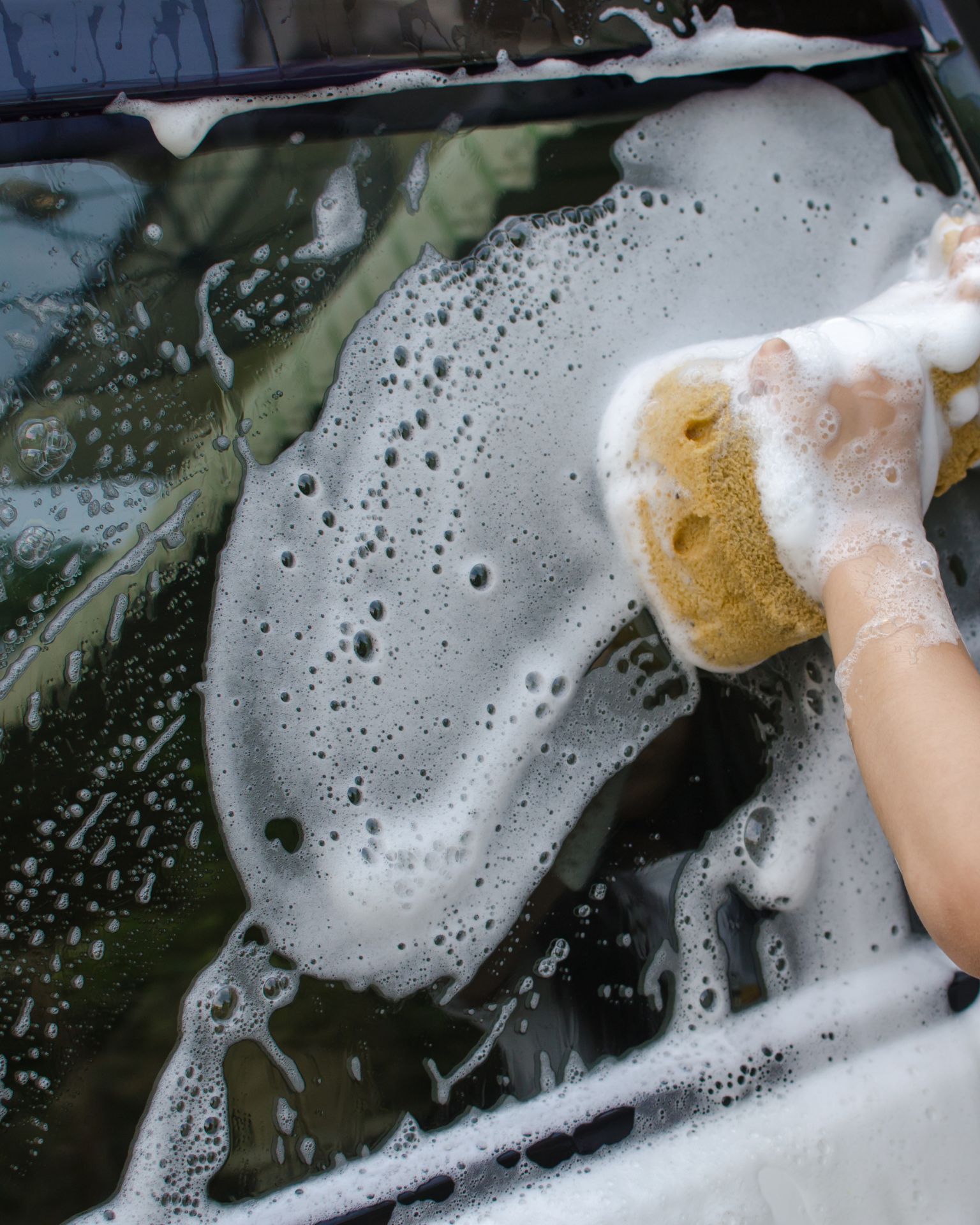 A man with tattoos is washing a car in a garage.