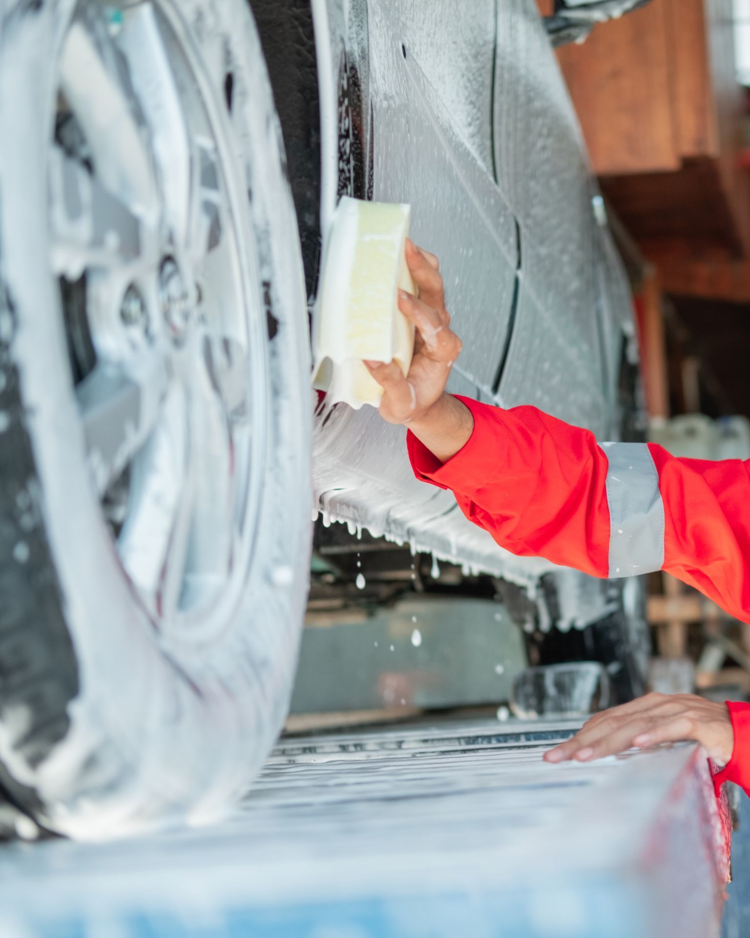 A man with tattoos is washing a car in a garage.