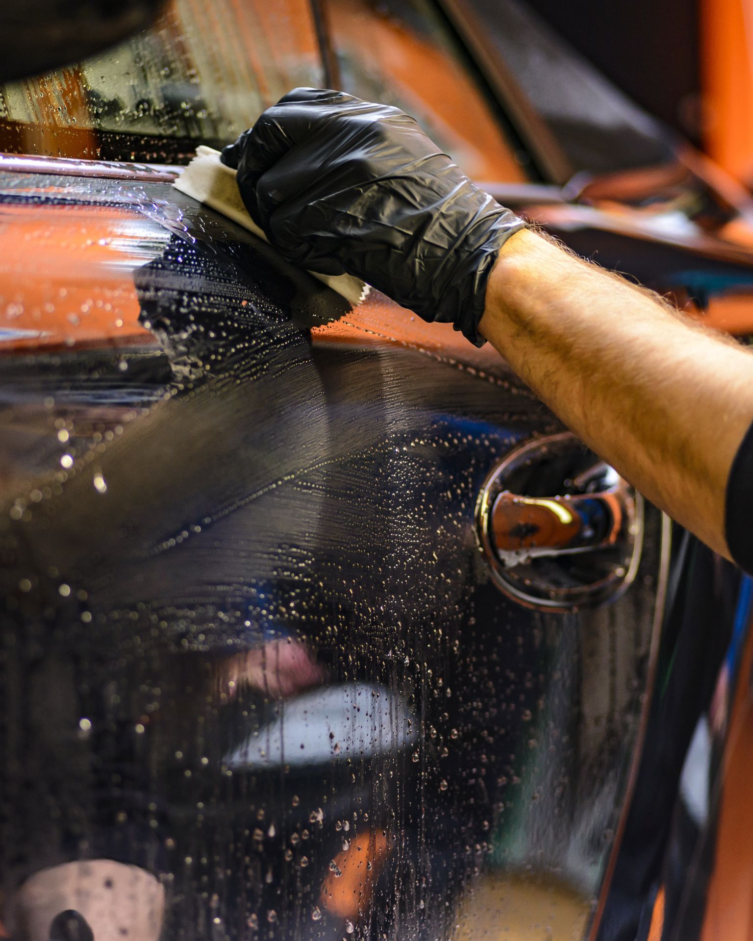 A man with tattoos is washing a car in a garage.