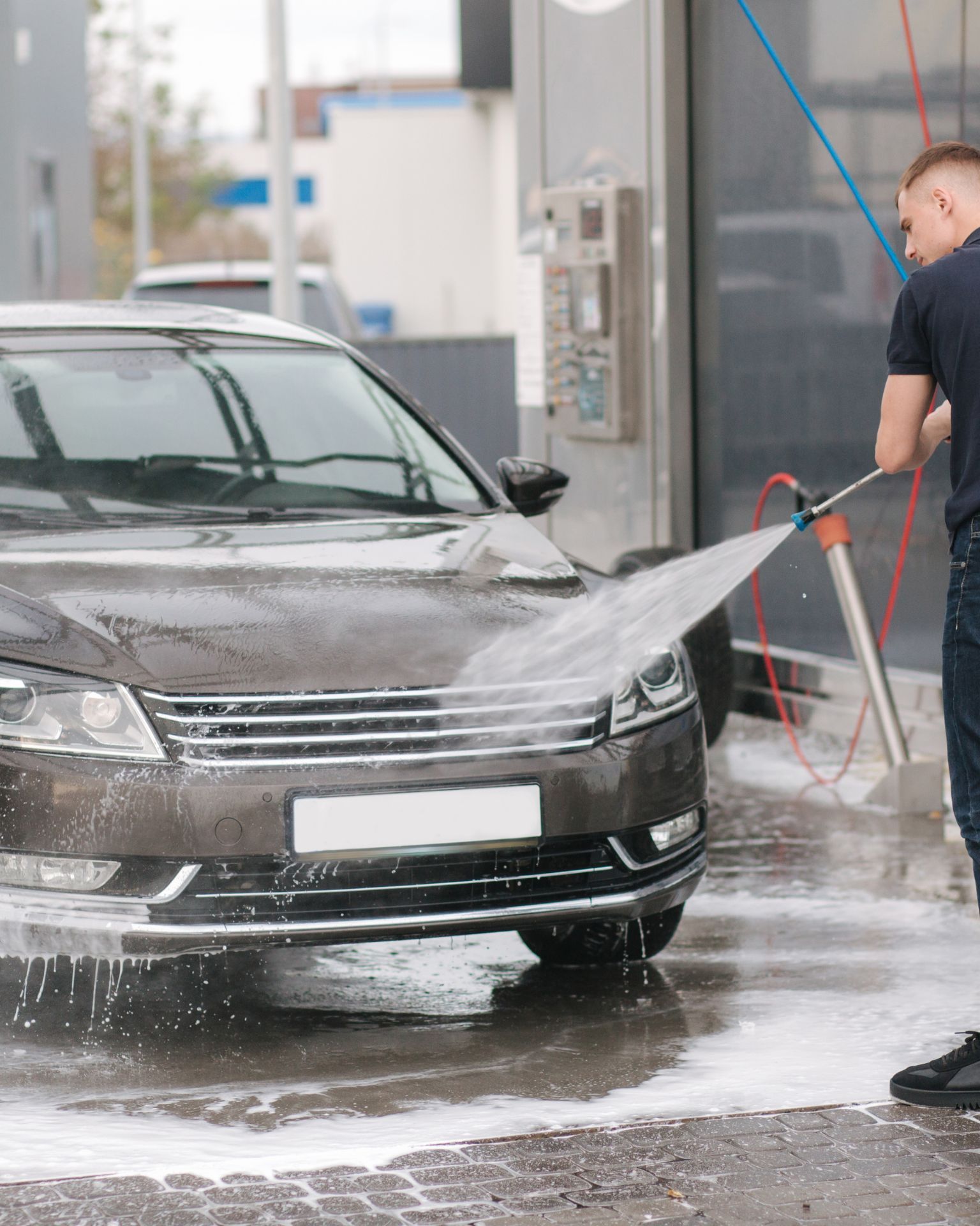 A man with tattoos is washing a car in a garage.