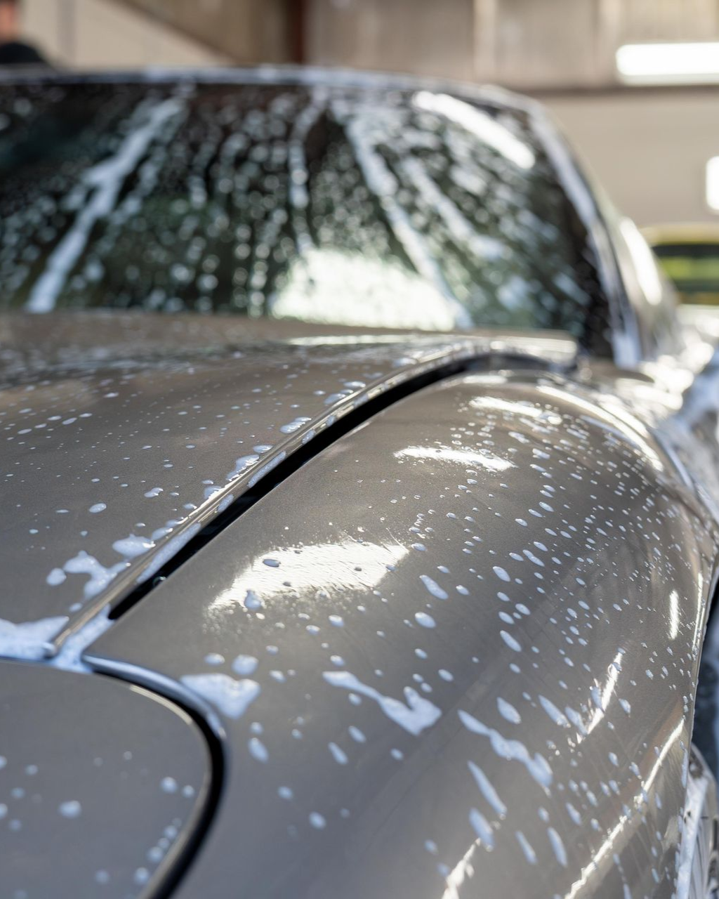A man with tattoos is washing a car in a garage.