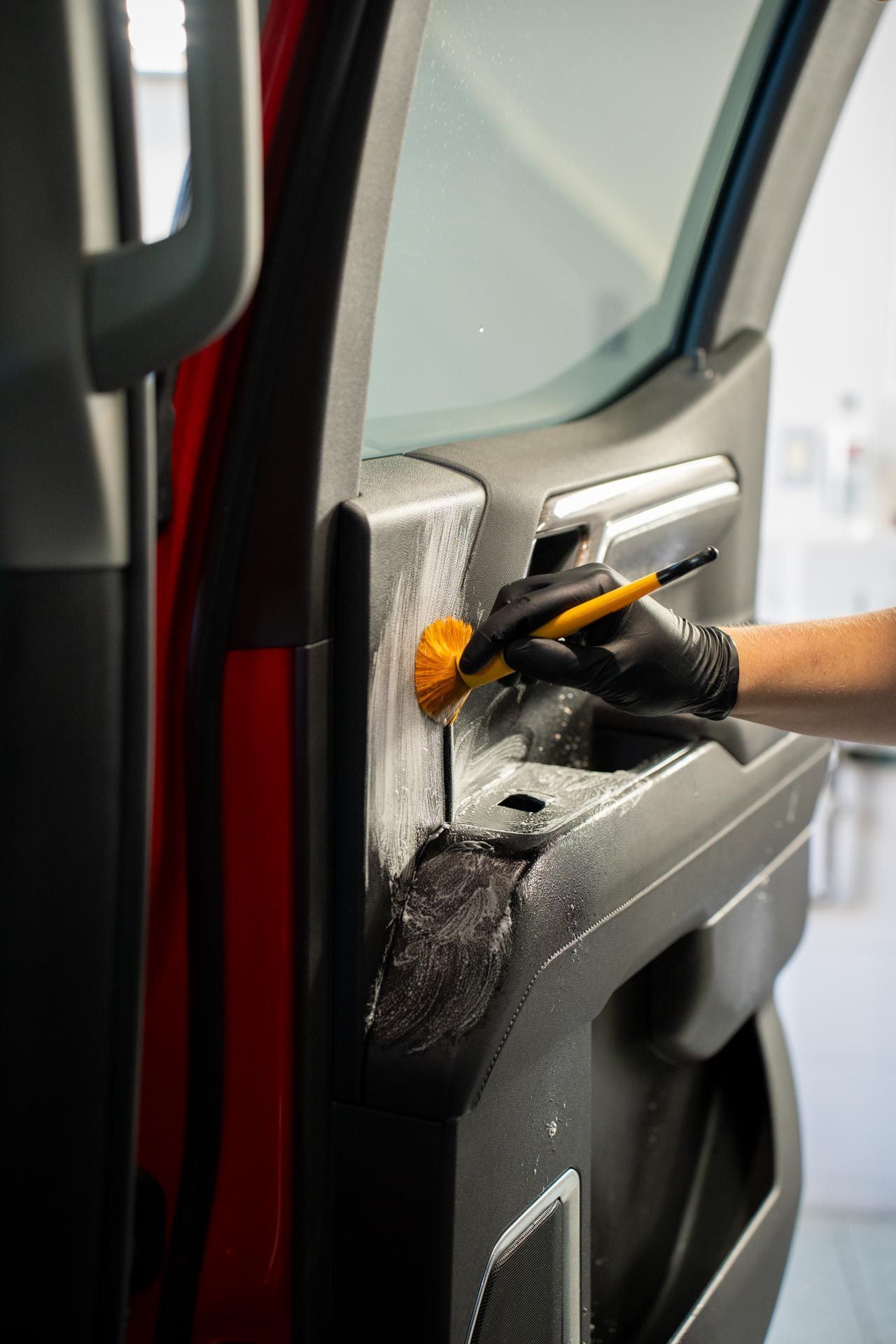 A person uses a pressure washer to clean the tire of a silver car inside a workshop with other vehicles.