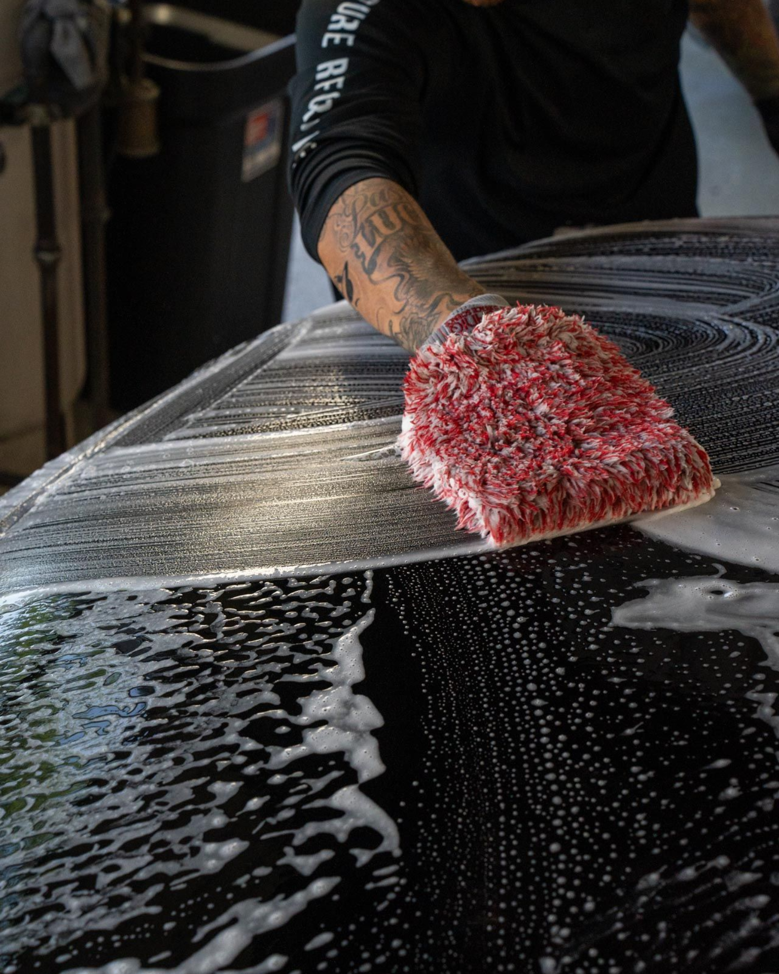A man with tattoos is washing a car in a garage.