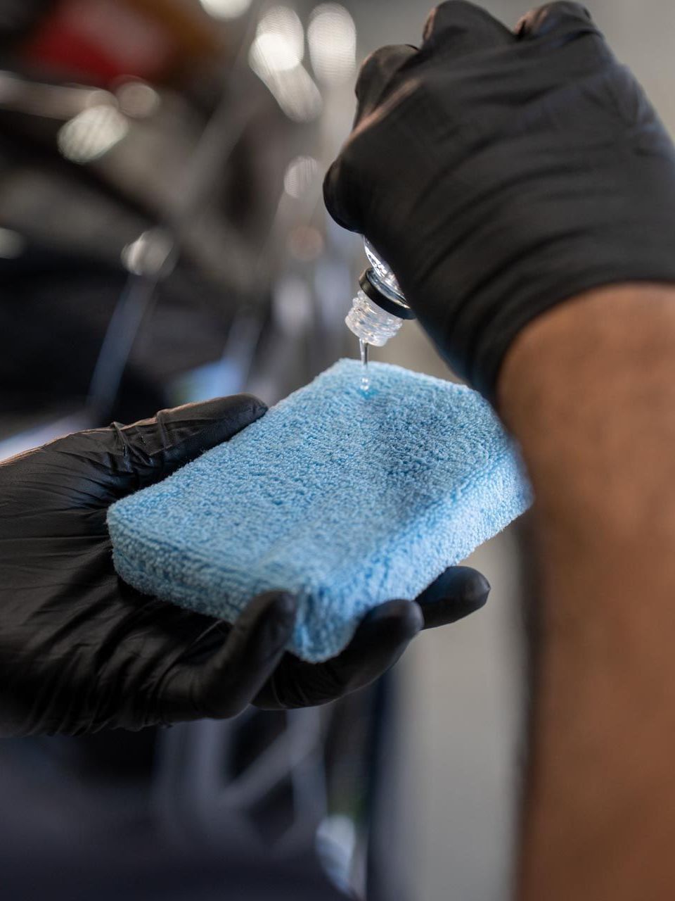A person wearing blue gloves is cleaning the headlight of a car